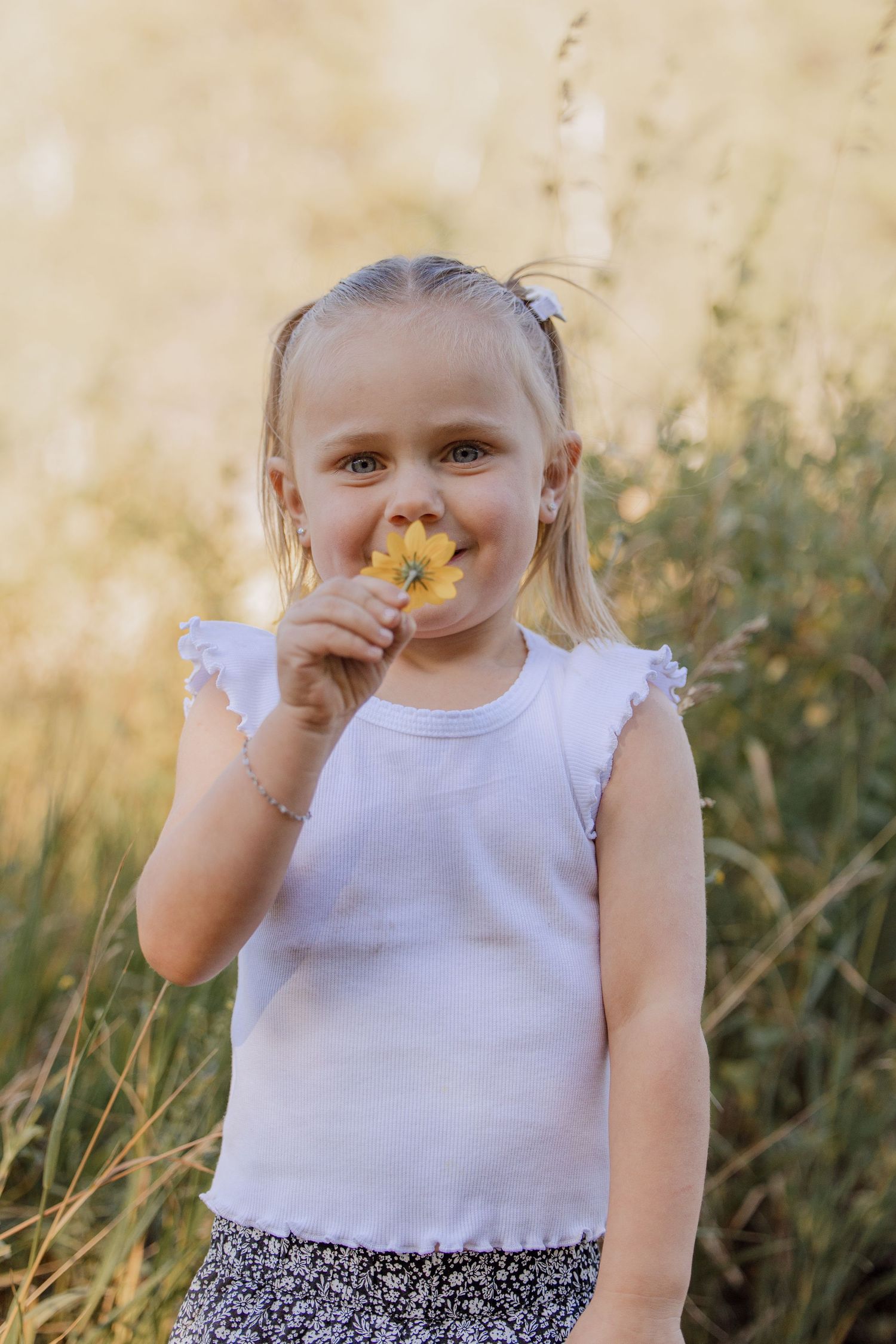 Child in white dress holding yellow flower in sunny meadow during golden hour.