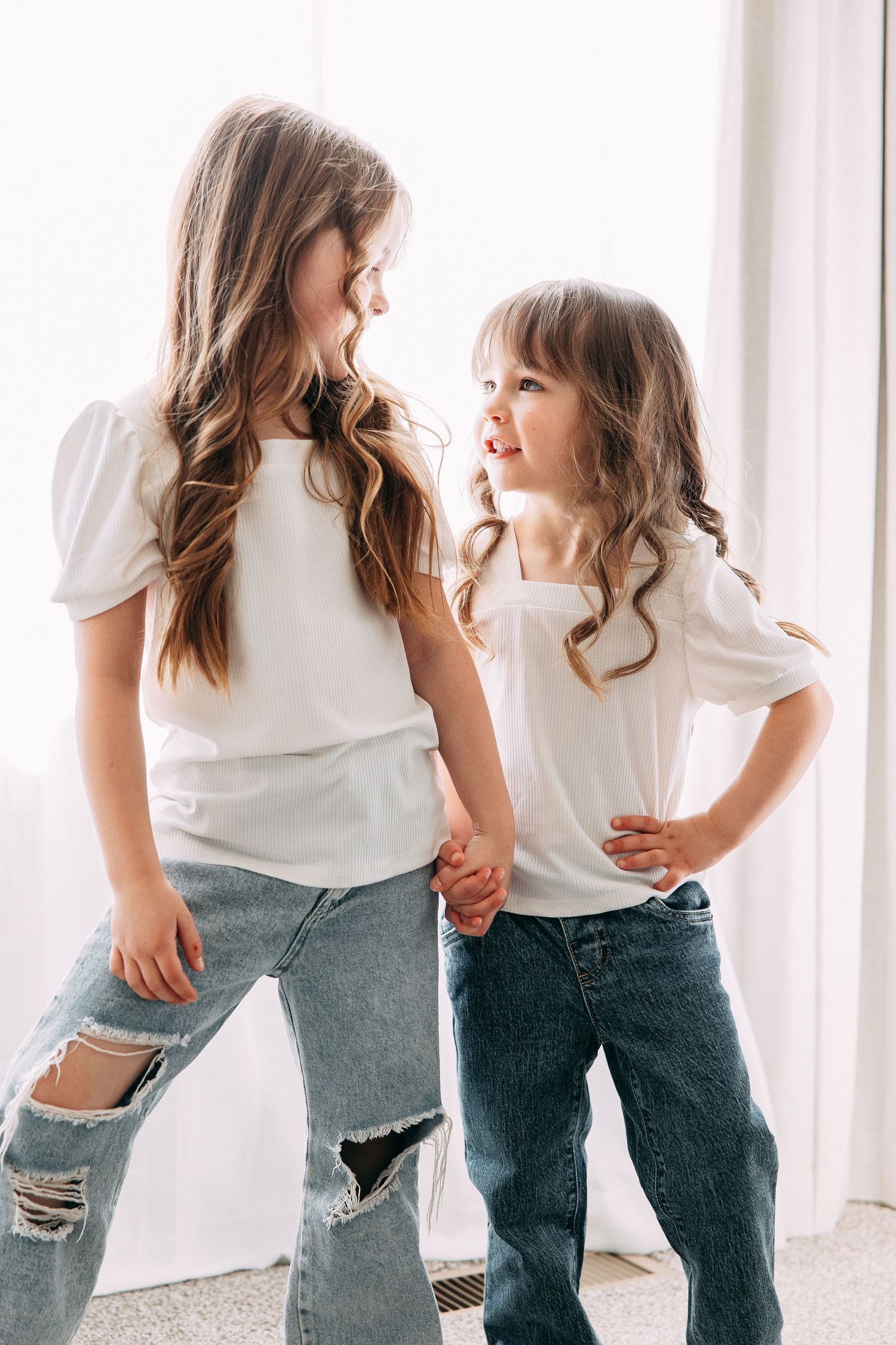 Children wearing matching jeans and white shirts pose playfully together.