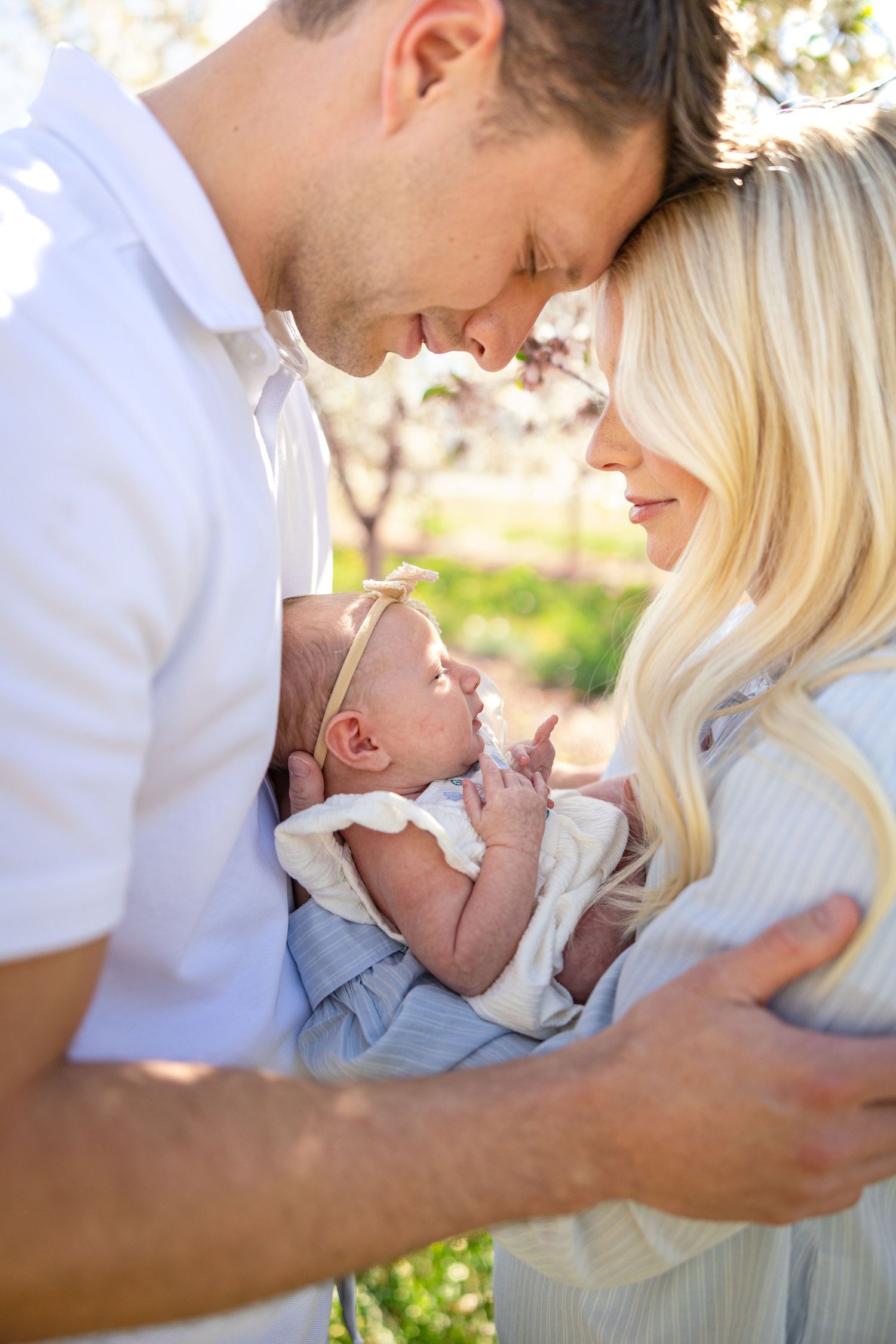 Family sharing tender moment with newborn baby in outdoor spring setting.