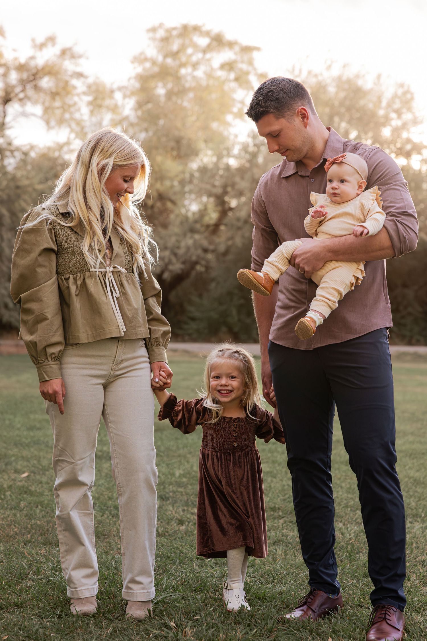 A casual family portrait taken outdoors in a park setting during golden hour.