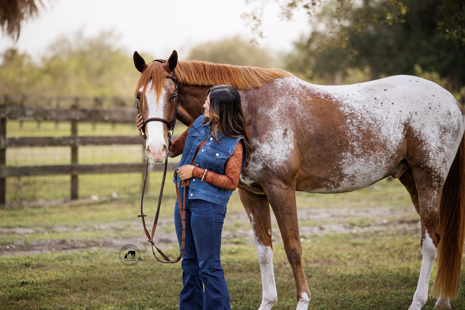 Two horses, one brown and one spotted, stand in a fenced pasture with someone in overalls.