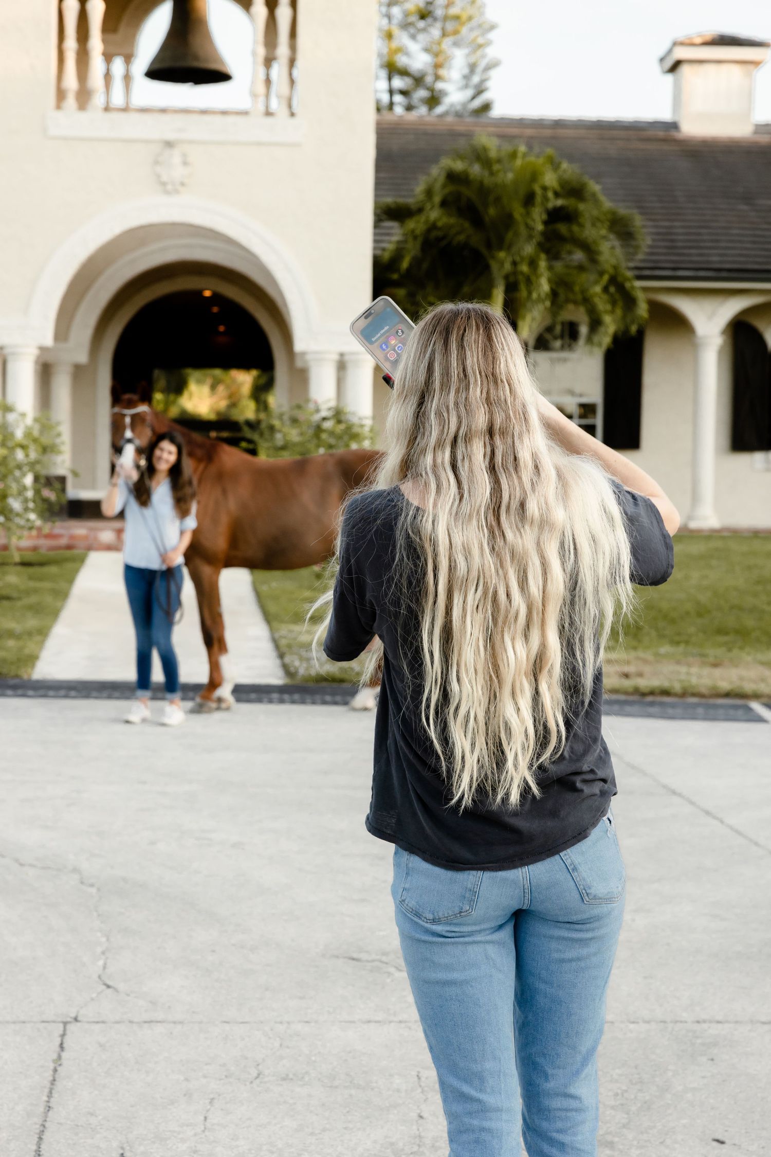 Woman in denim taking photos with a white horse at a rustic stable location.