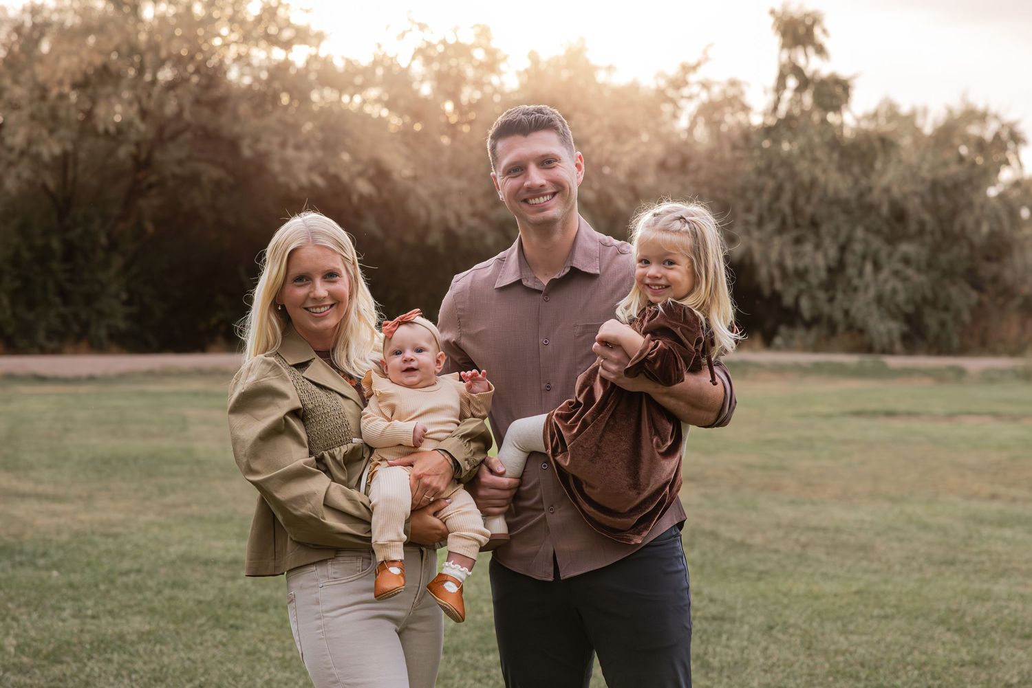 A family portrait taken outdoors at sunset in a grassy field.