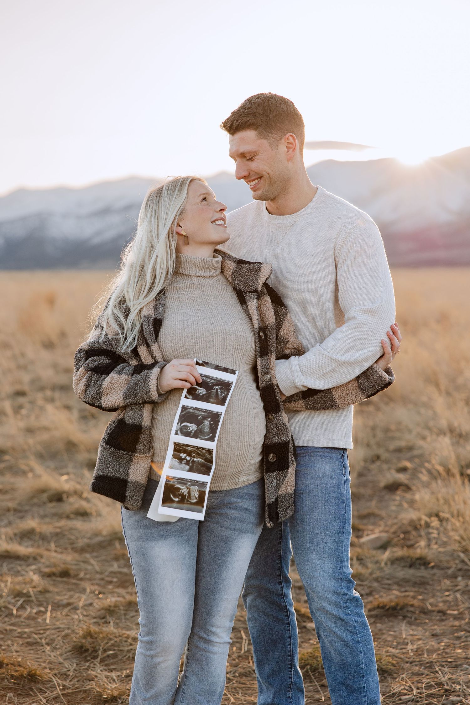 Couple shares intimate moment while holding ultrasound strip in outdoor mountain setting.