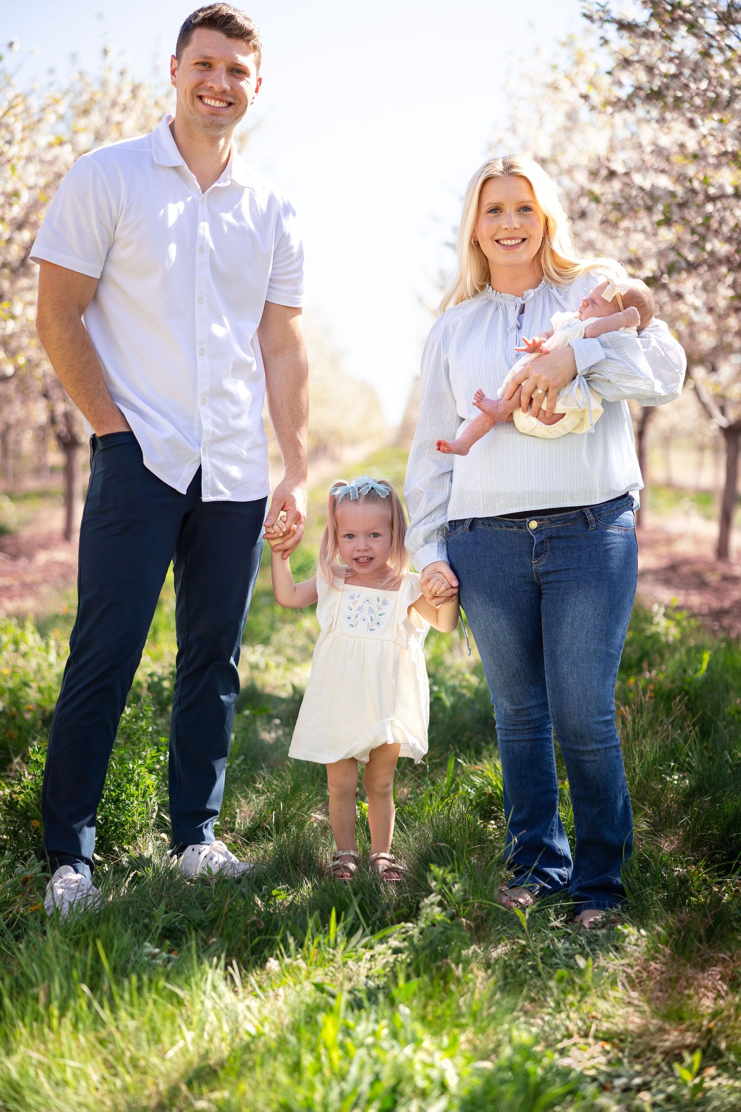 Family walking together through blooming orchard during spring photo session.