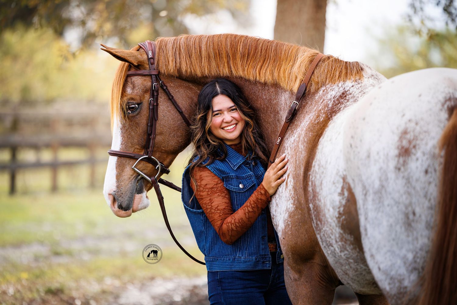 A brown horse and rider in denim vest share a joyful moment in an autumn setting.