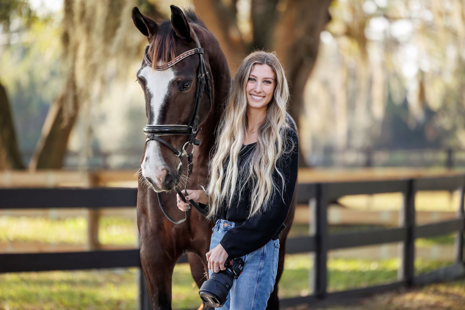 A horse and companion pose together on a fall day with trees and wooden fencing in the background.