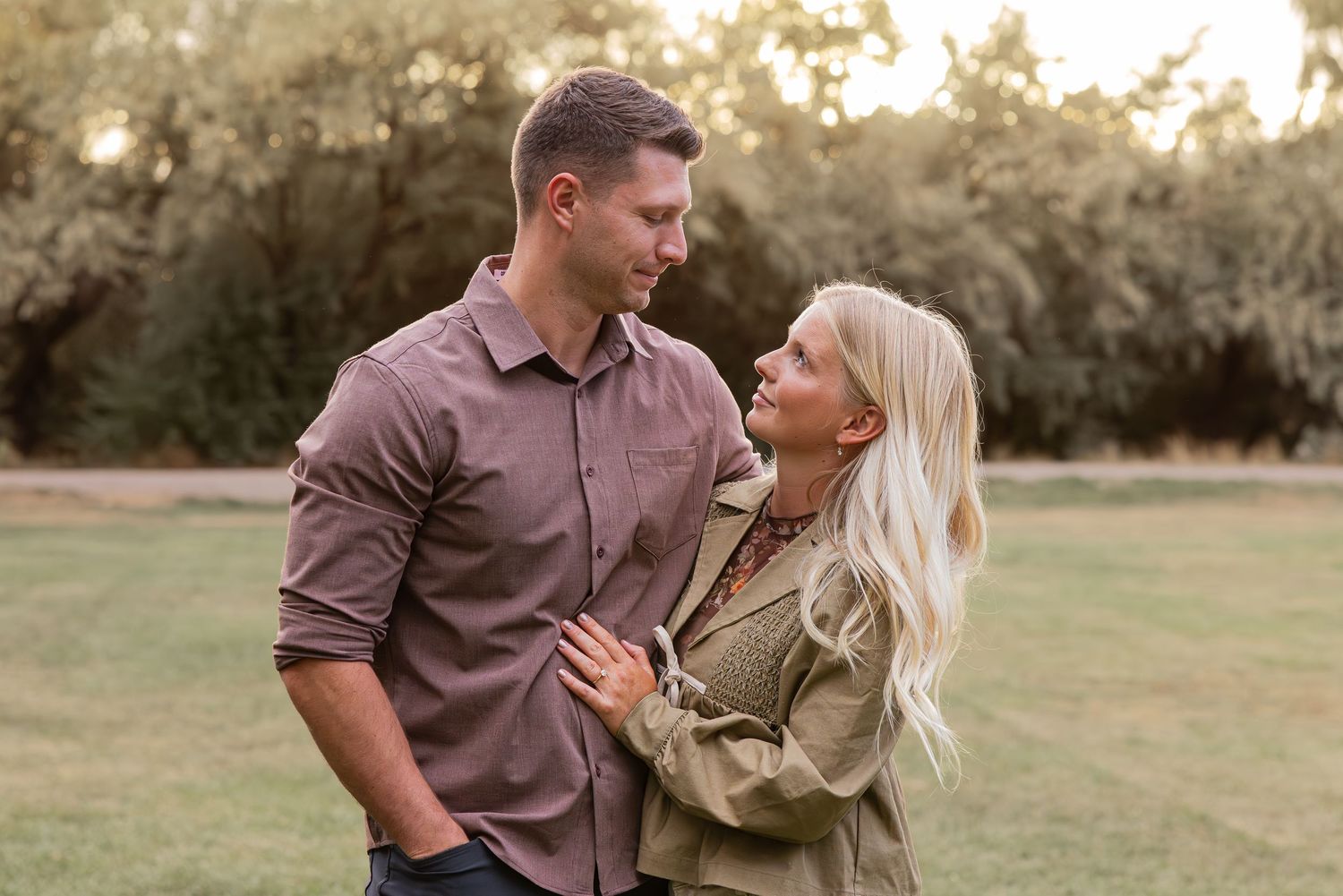 A couple shares an intimate moment while posing outdoors at sunset.