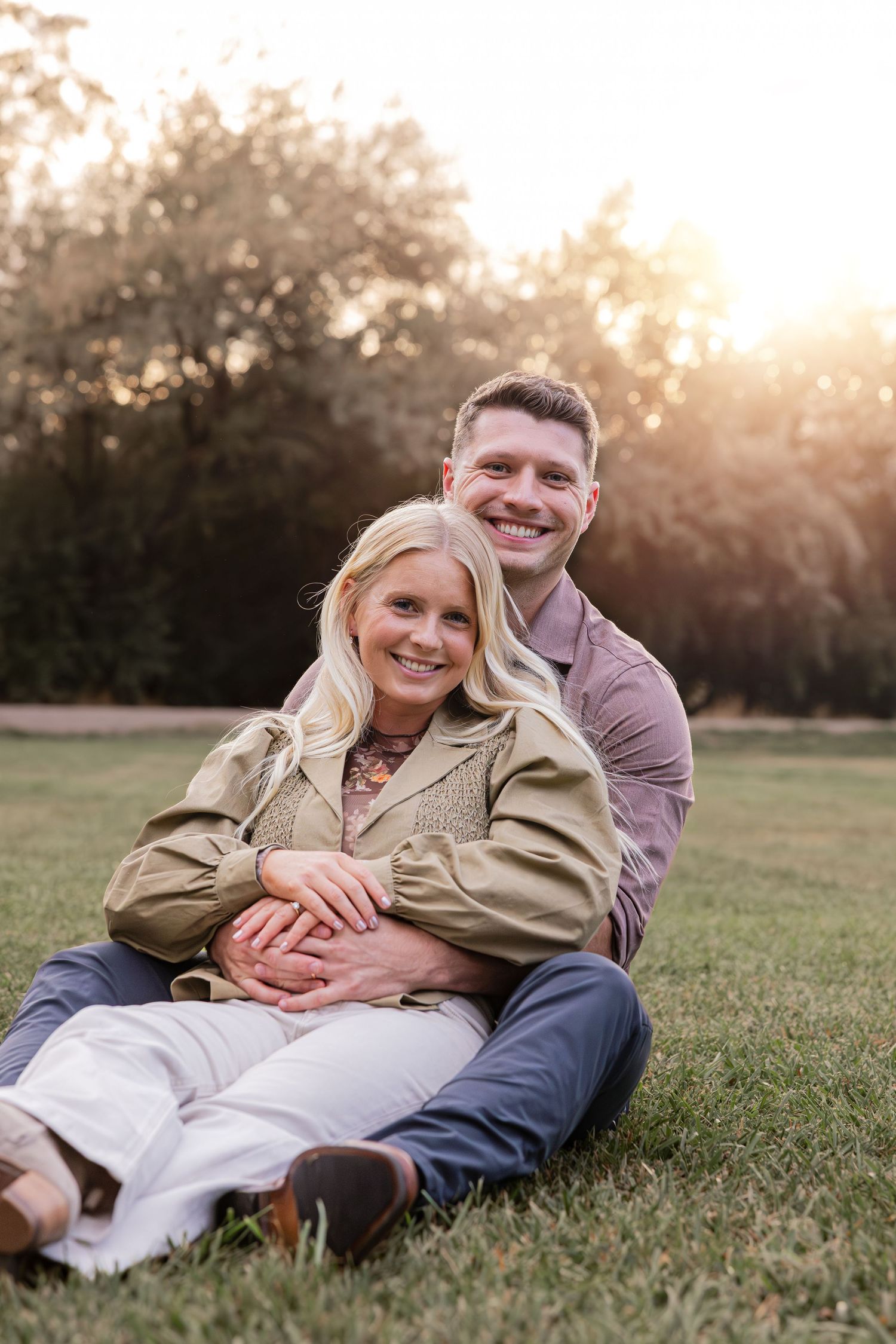 Couple lying together on grass during golden hour sunset in a romantic outdoor photoshoot.