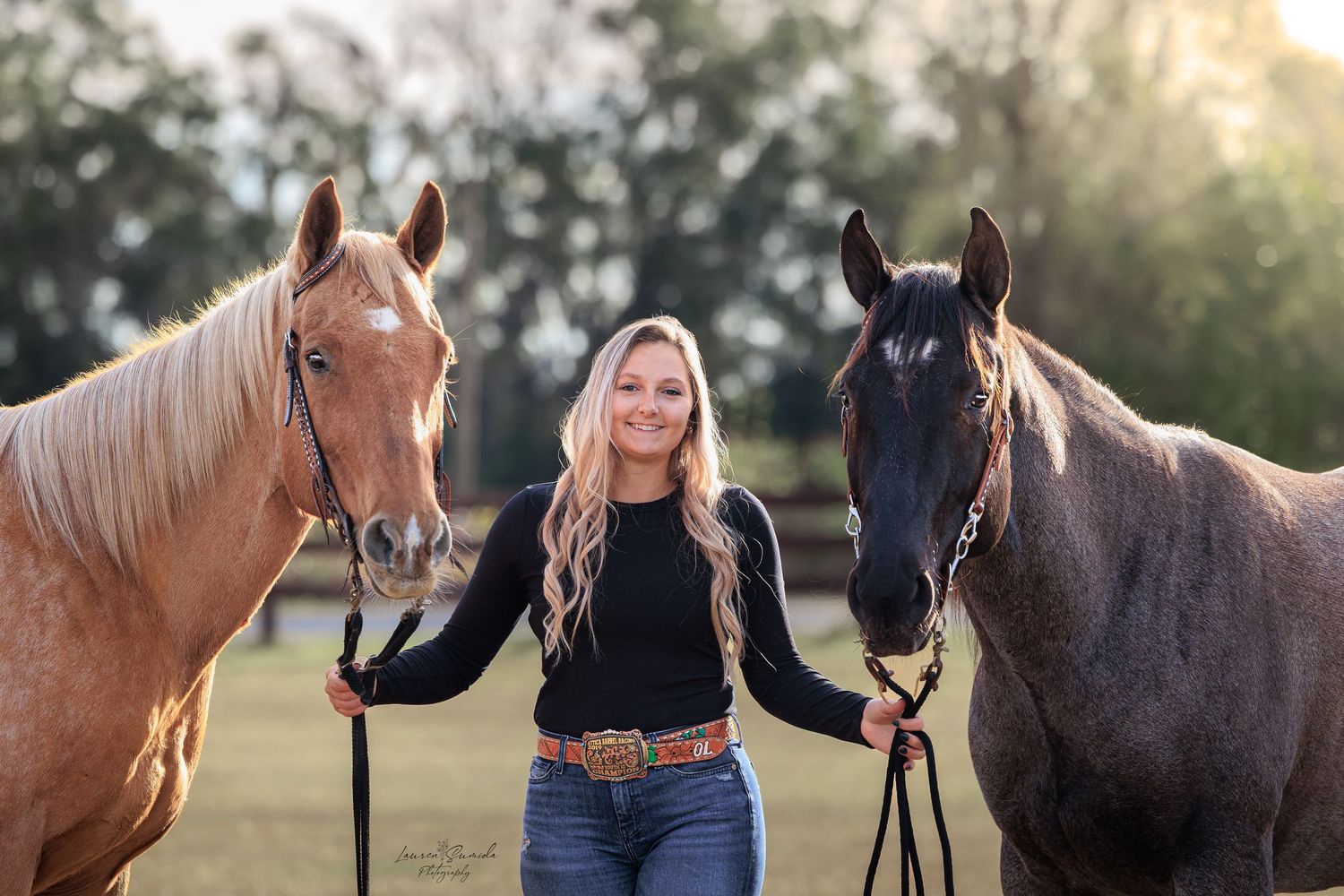 Horses and handlers stand together in a grassy field during sunset creating a peaceful outdoor scene.