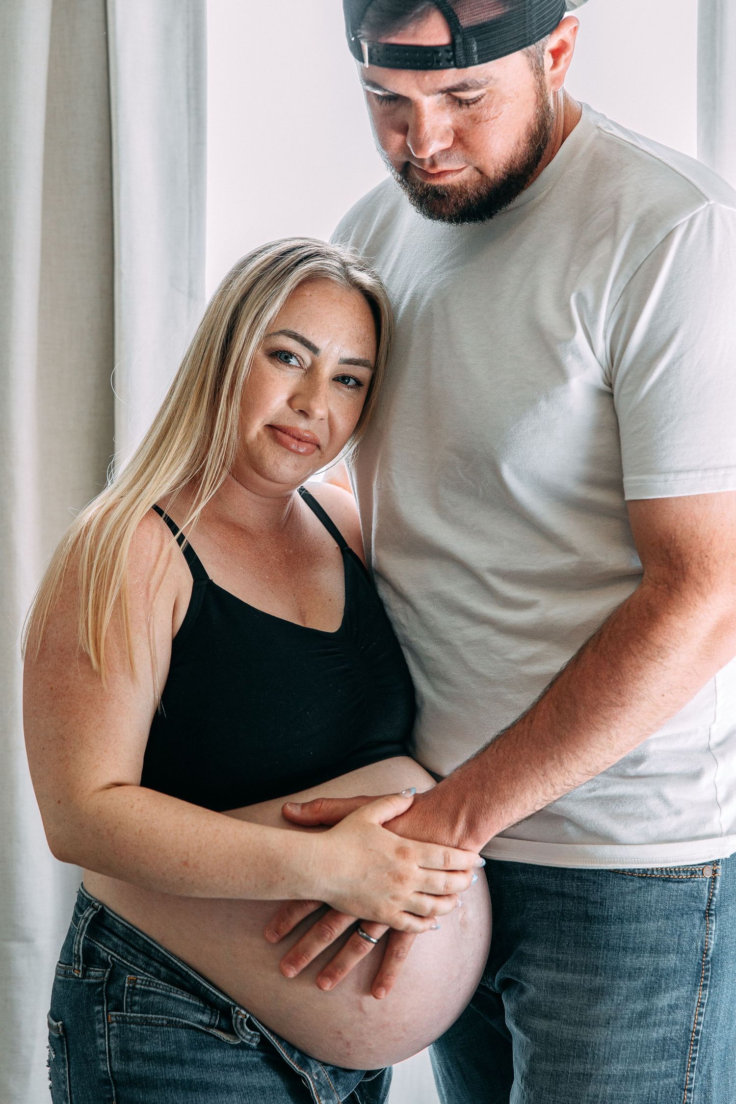 Candid moments of an expecting couple sharing embraces by a window.
