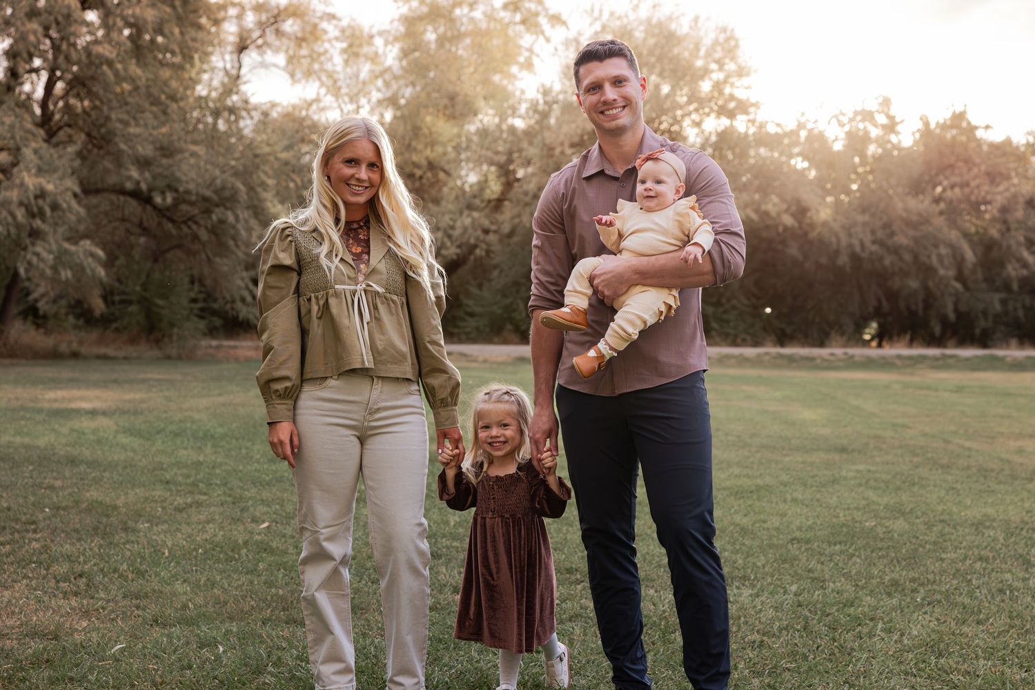A family stands together on grass during sunset for a portrait session.