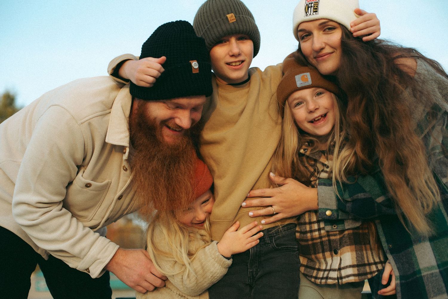 A group of friends laugh and embrace while enjoying time together outdoors on a sunny day.