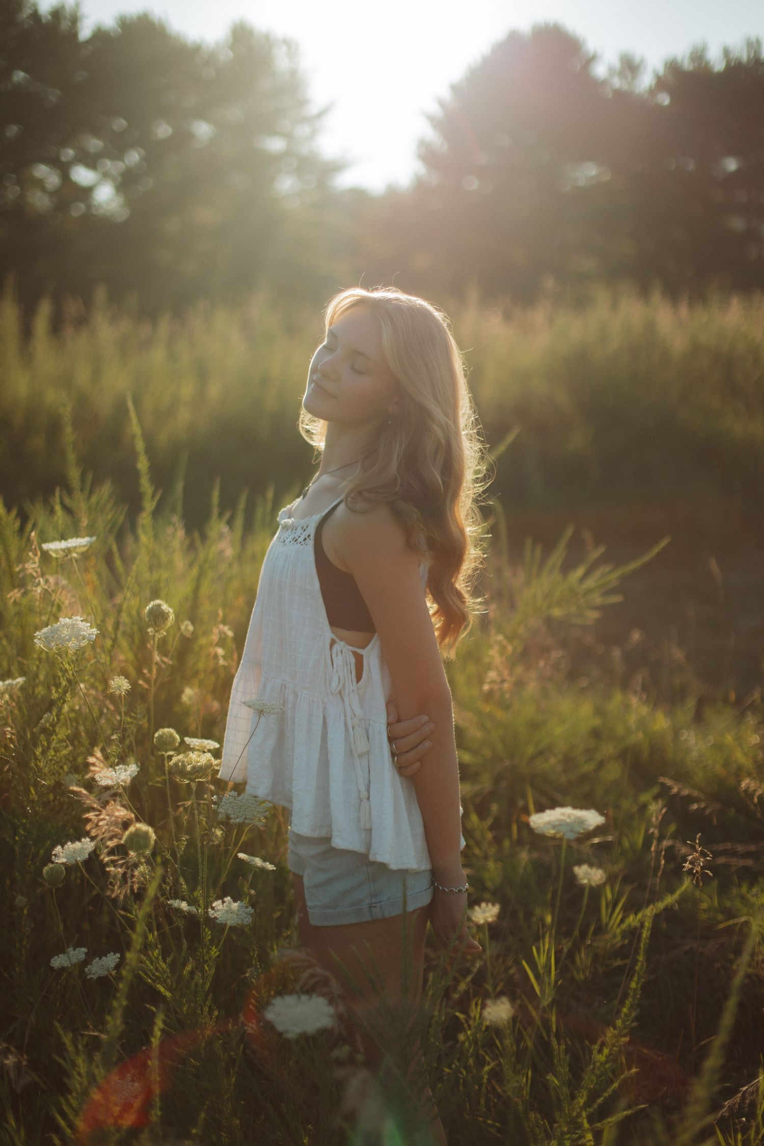 Person in white dress standing in a wildflower field during golden hour sunset.
