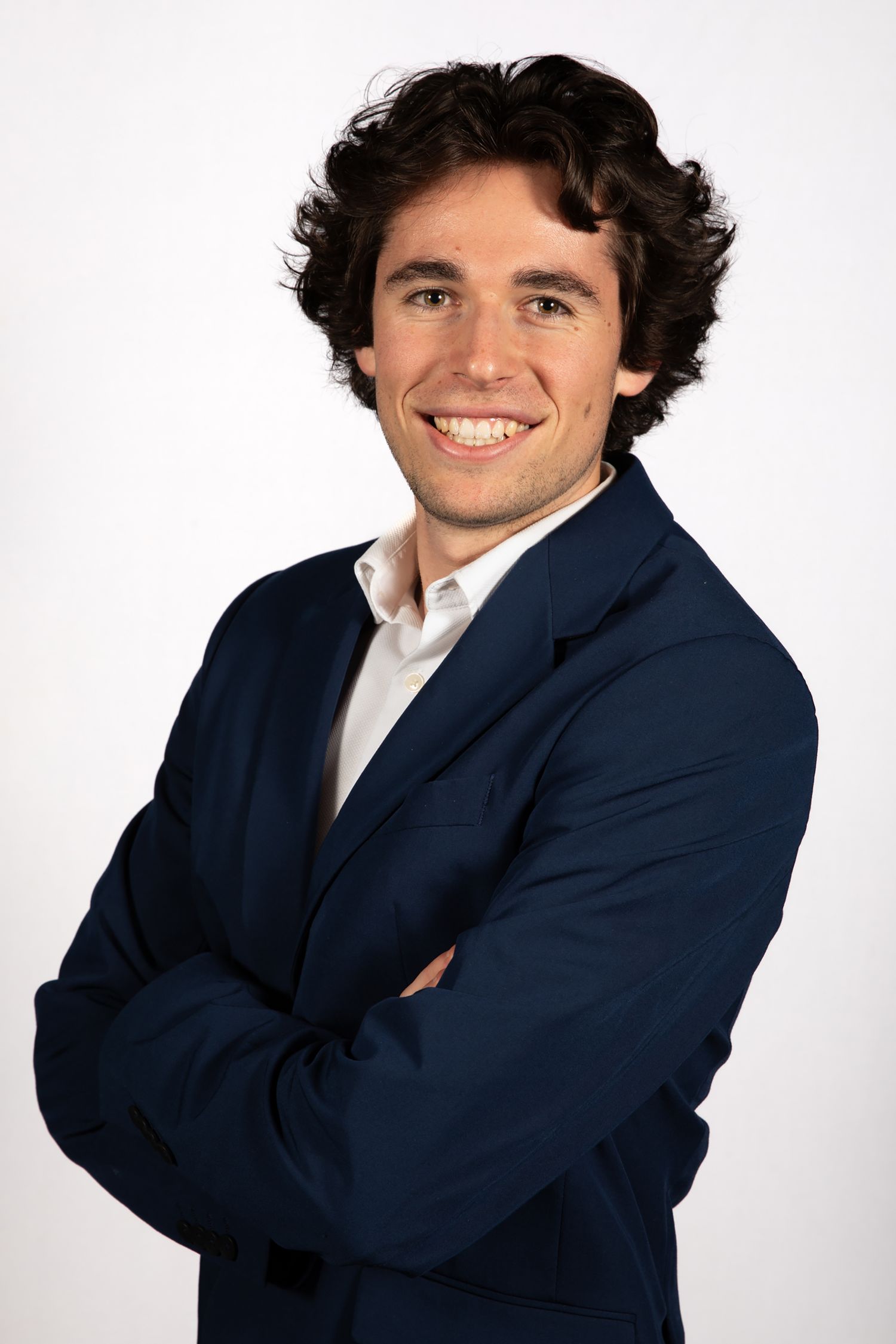 Professional portrait of someone in a navy suit and white shirt against white background.