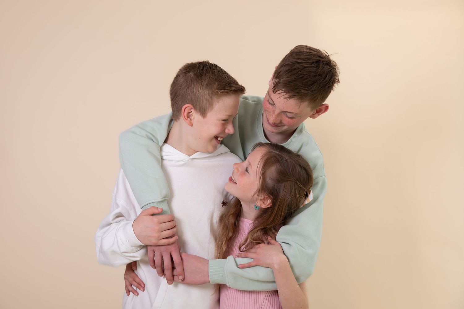 A father hugs his son and daughter warmly against a beige background in a joyful family portrait.