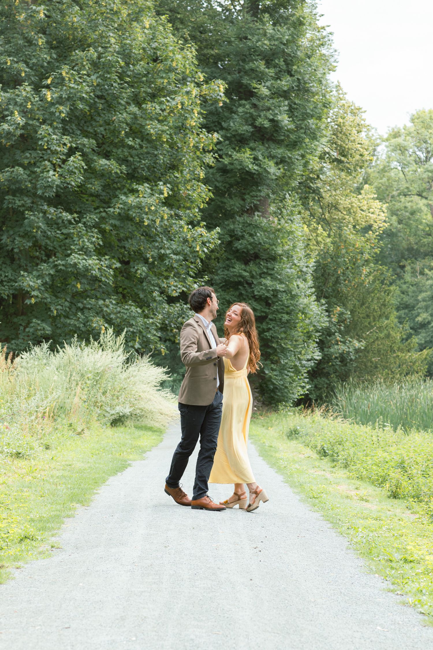A couple dancing and twirling on a gravel path surrounded by lush green foliage.