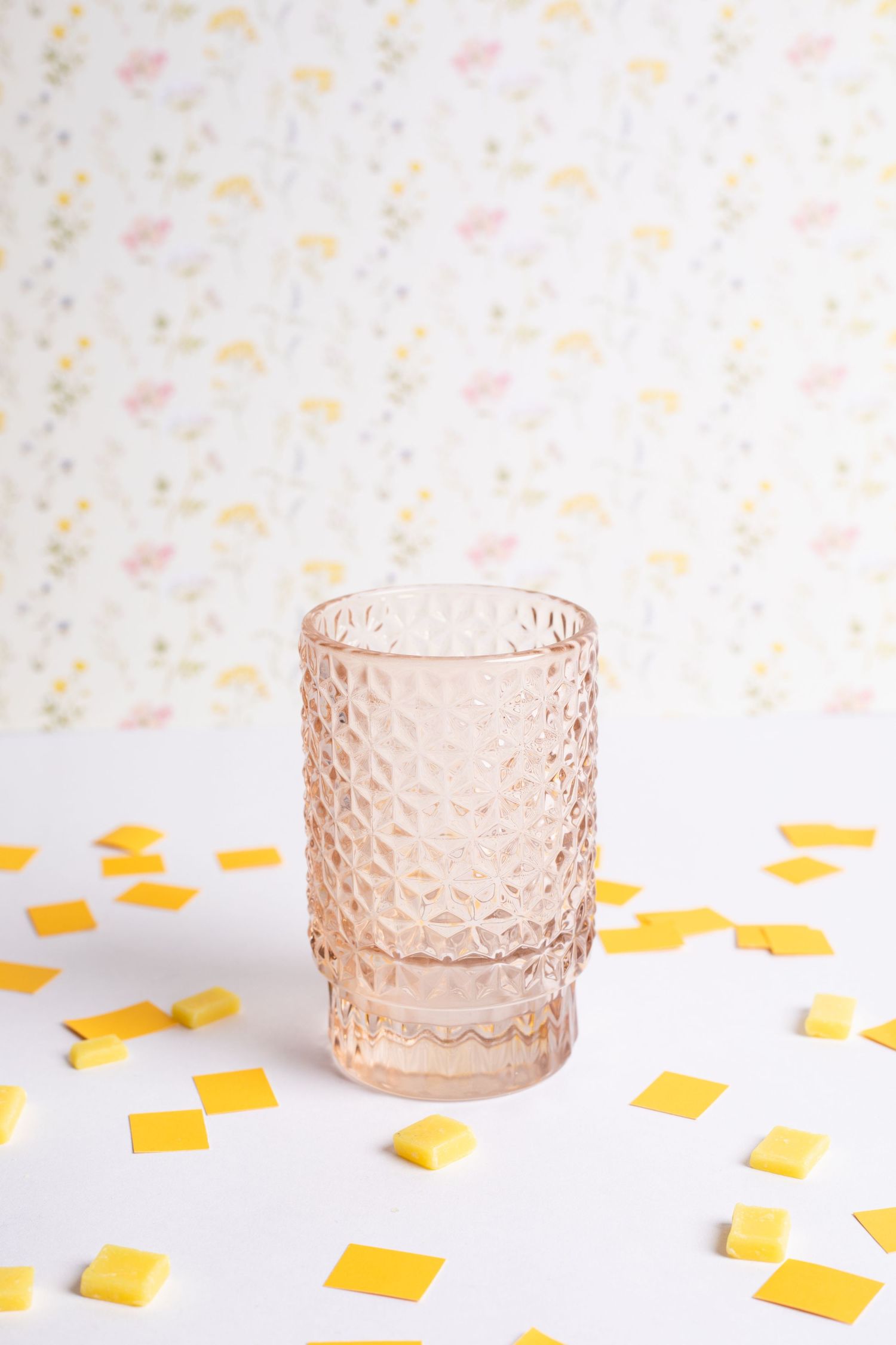 Pink textured glass tea light holders arranged in a row with scattered yellow paper confetti on white surface.