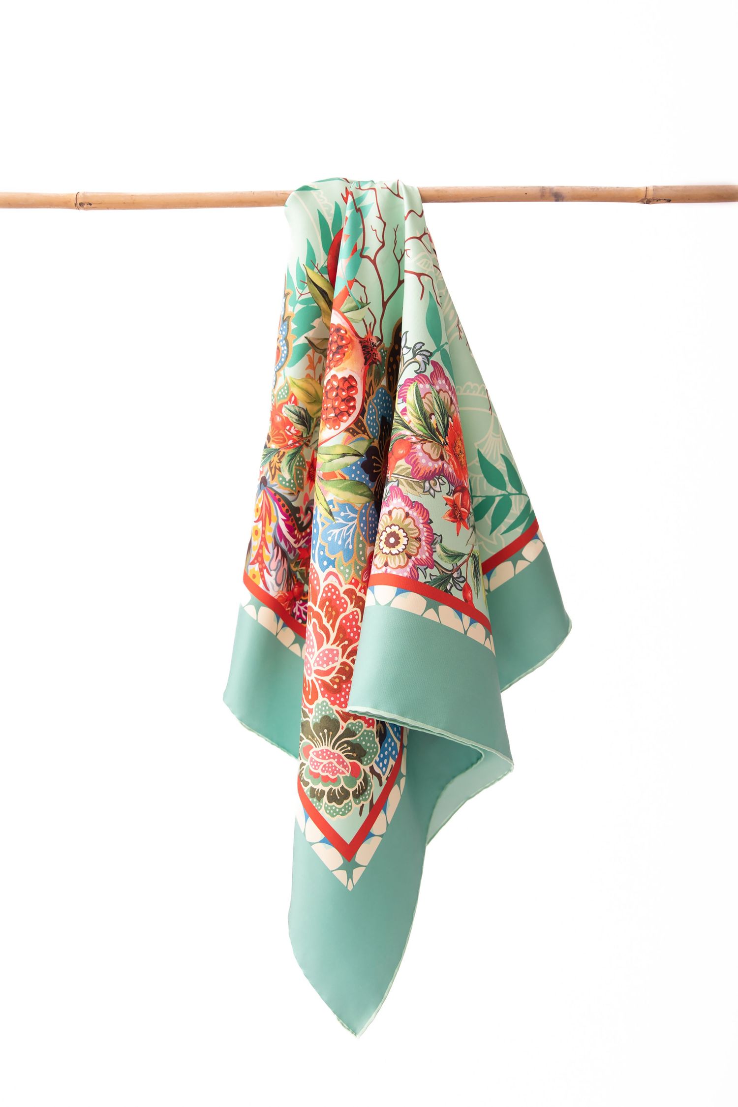A vintage floral pattern scarf in mint green and coral pink hangs elegantly on a wooden rod against a white background.