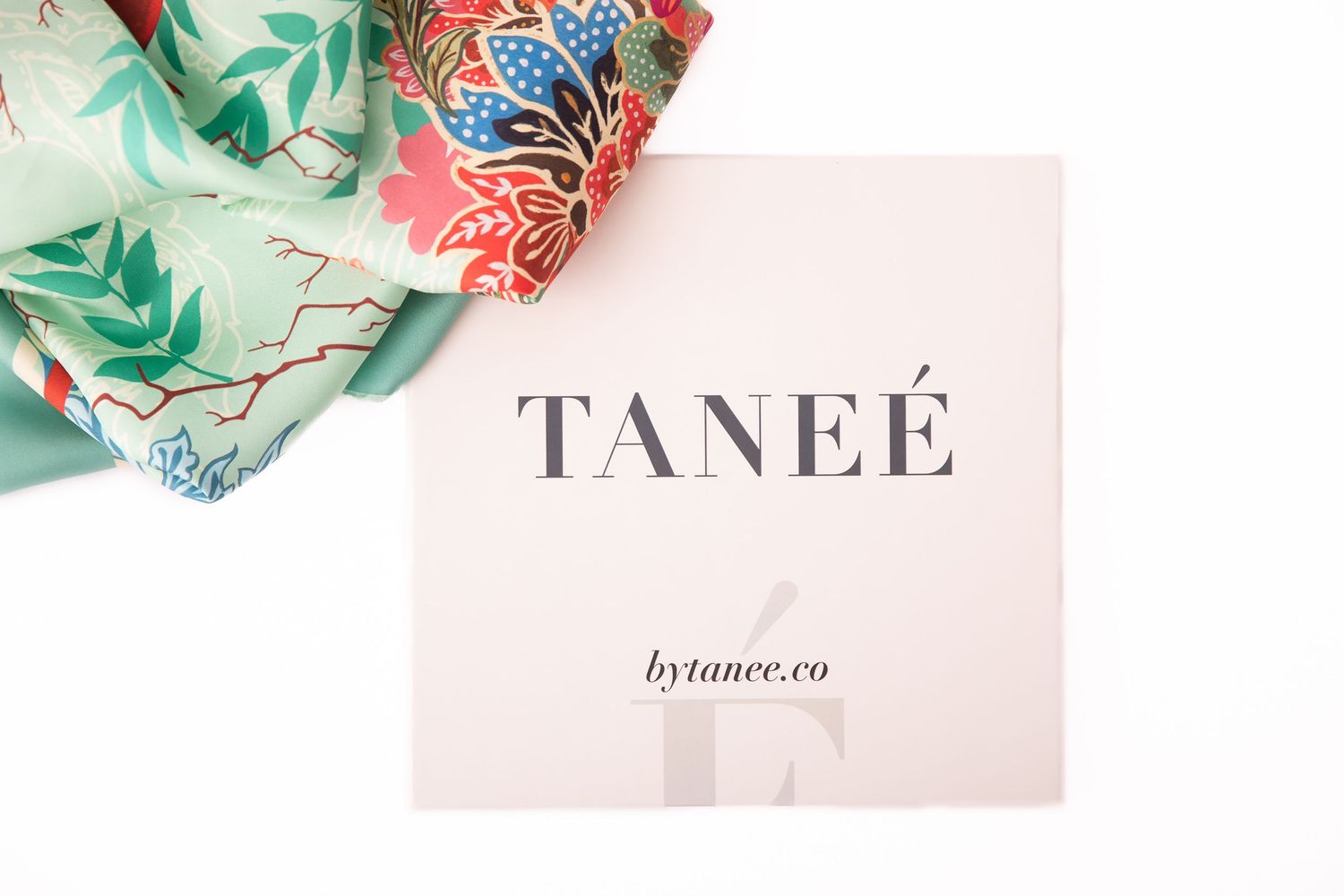 A TANEÉ branded card with bytanee.co logo beside a colorful floral silk scarf on a white background.
