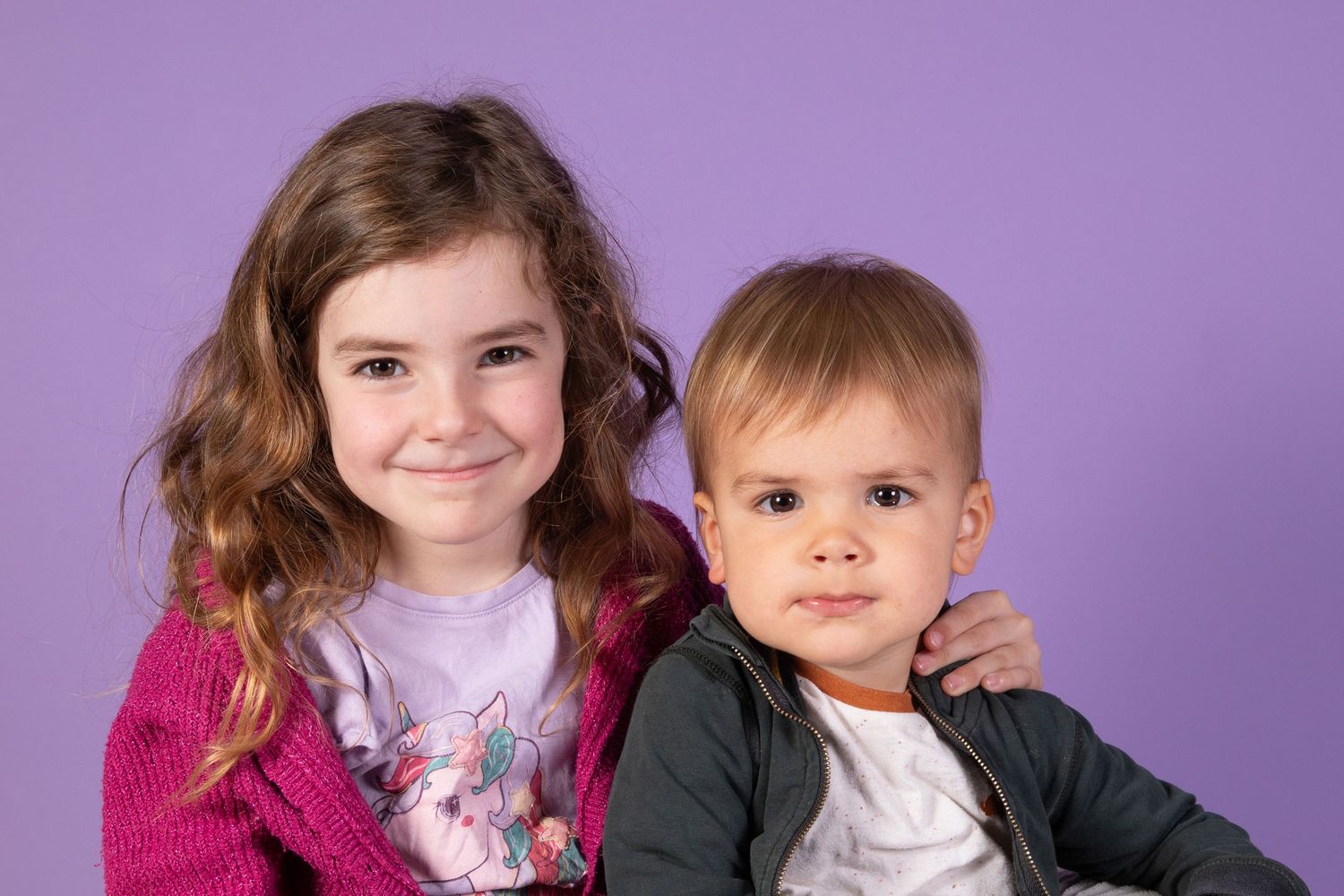 Children posing together against purple backdrop in coordinated outfits.