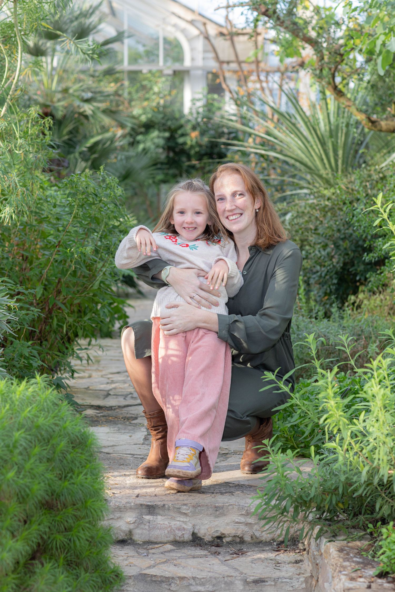 Family photo session in a lush greenhouse garden setting.