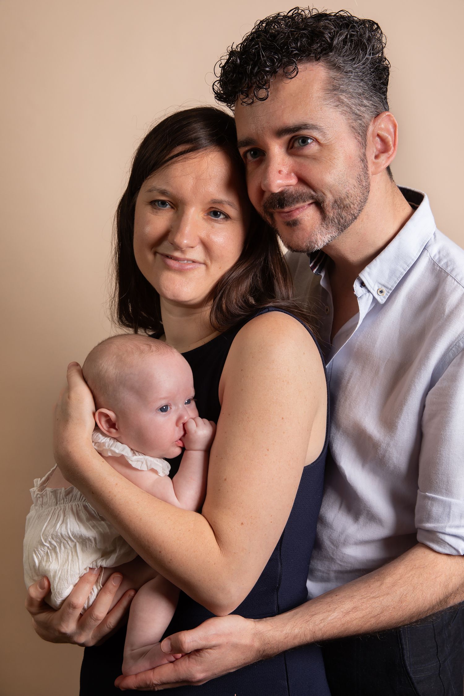 A series of intimate family portraits showing tender moments between parents and their baby against a neutral backdrop.