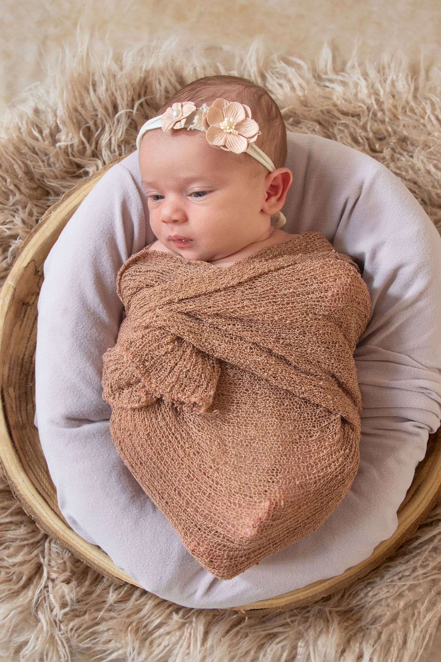 Newborn baby sleeping peacefully in brown wrap on plush fur backdrop.