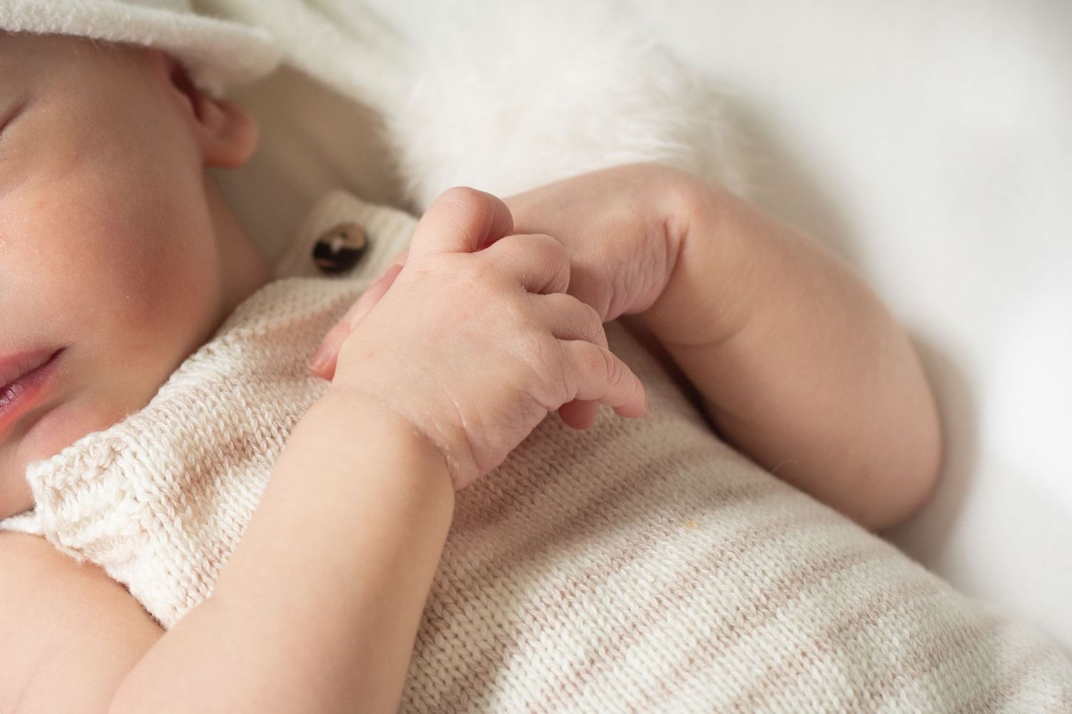Close-up of tiny infant hands grasping white knit fabric.