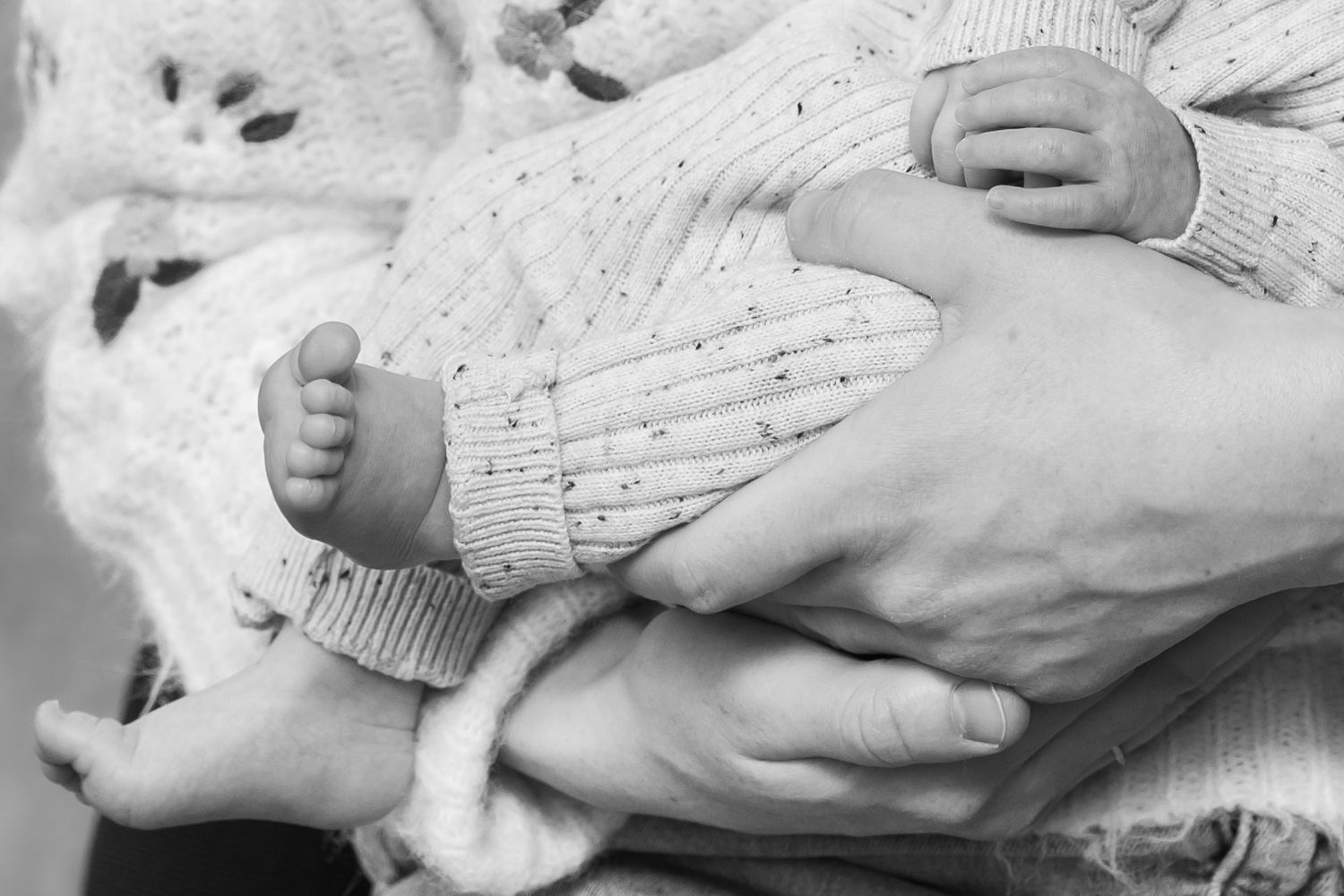 Black and white photo of a newborn baby being cradled in adult hands, showing tiny feet and fingers.