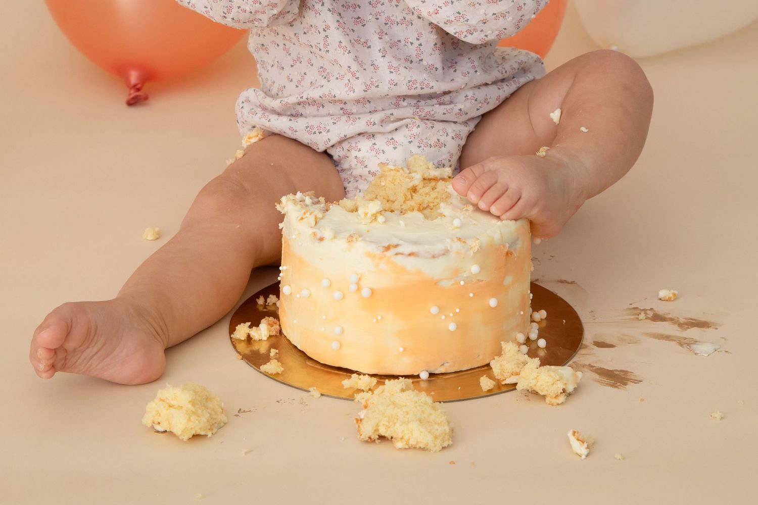 Smashed cake scene with scattered crumbs and frosting on beige background.