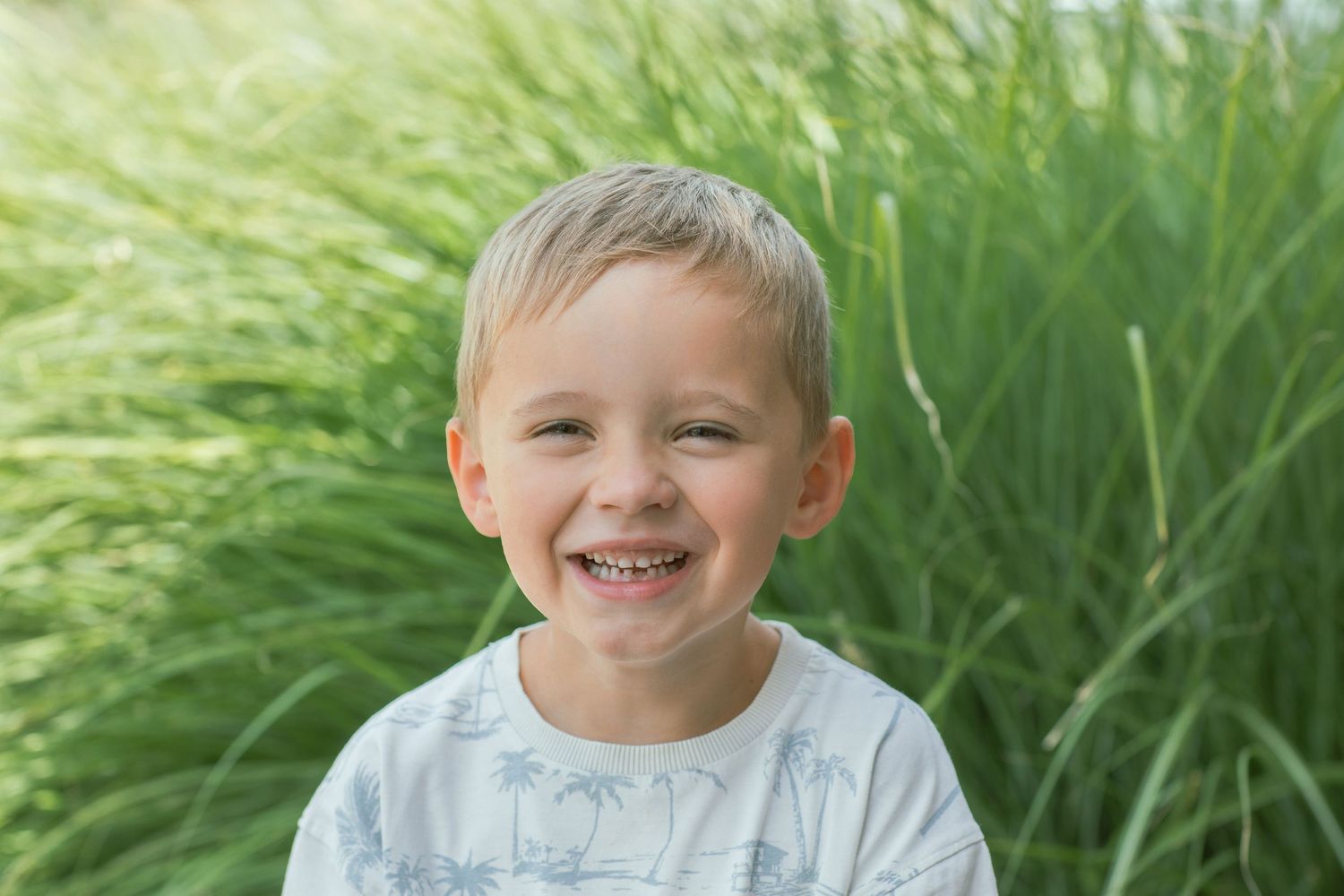 Young child smiling brightly while sitting in tall green grass during summer.