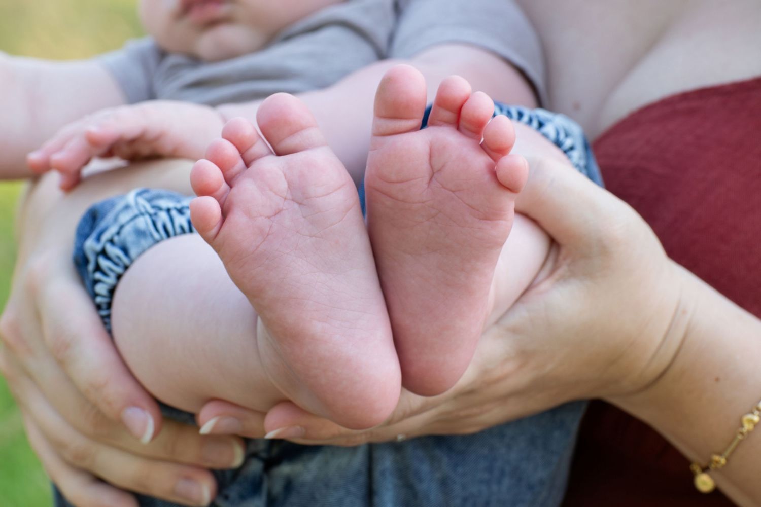 Close-up of a parent holding a newborn baby's tiny feet in their hands outdoors.