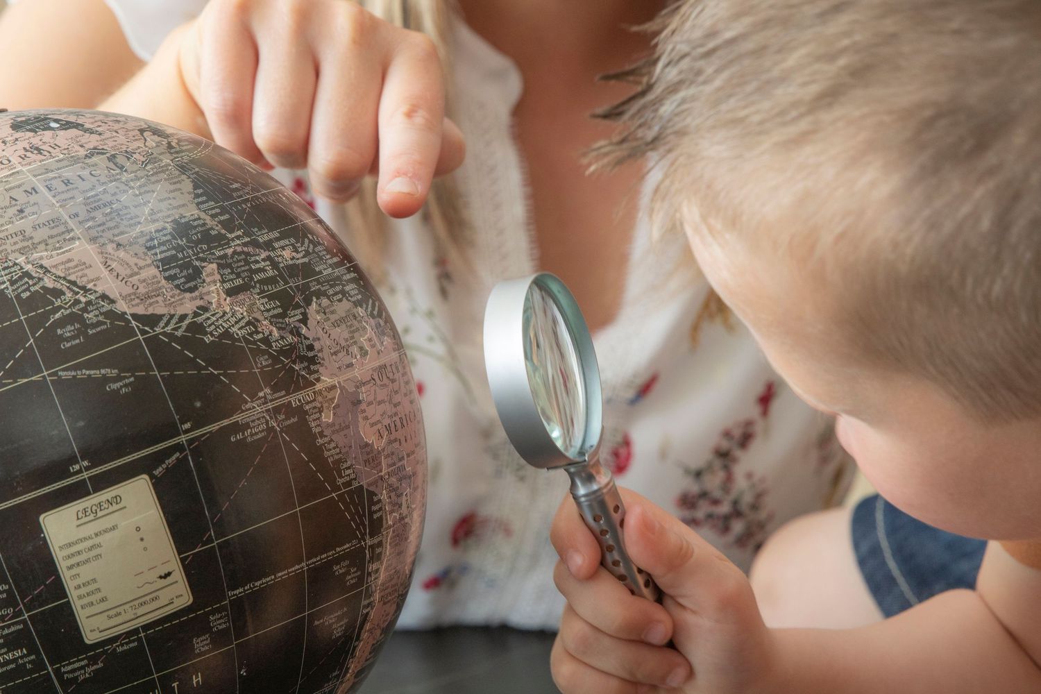 Close-up of hands examining details on a map with magnifying glass.
