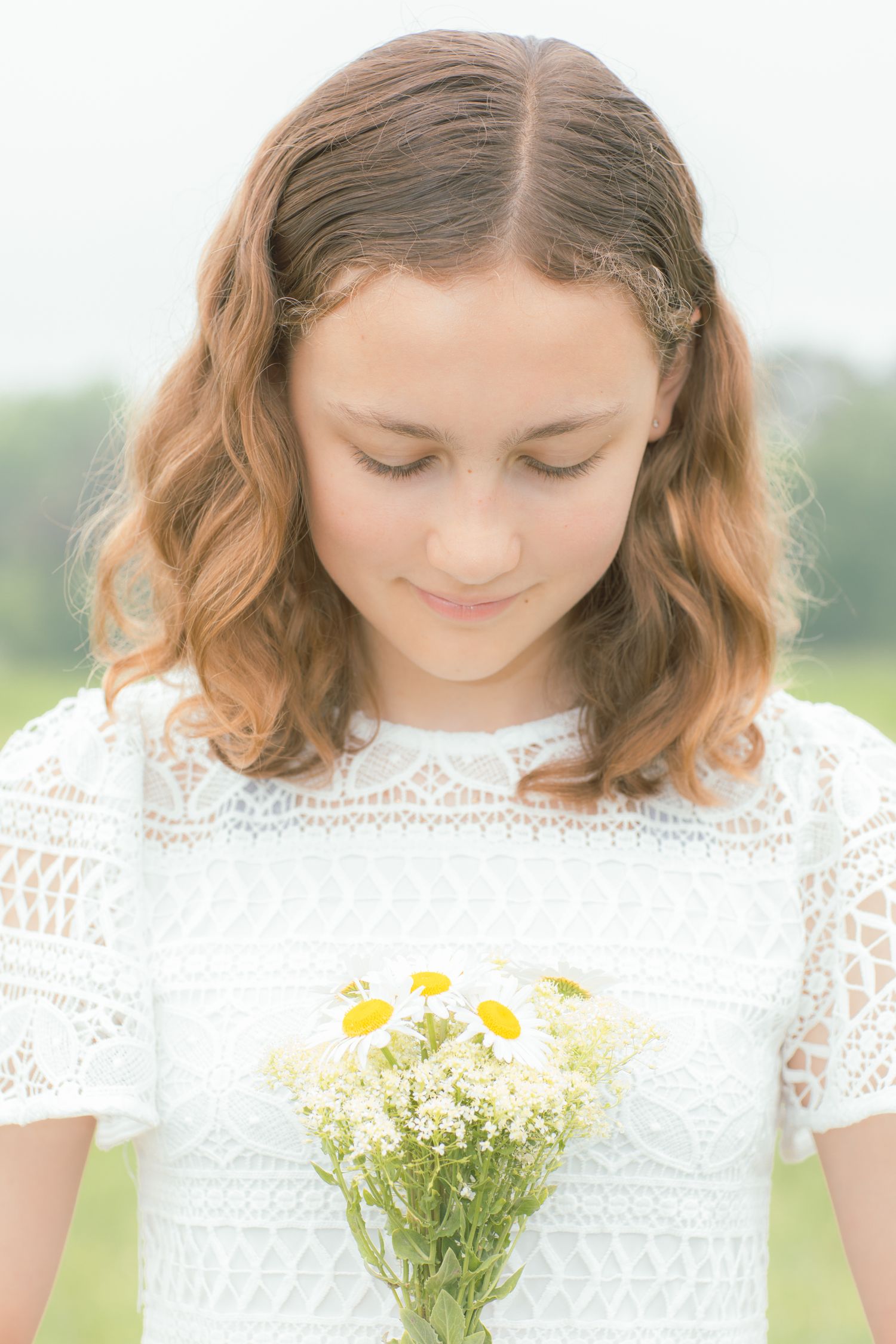 A person in a white lace dress holding a bouquet of fresh daisies and wildflowers in a sunny outdoor setting.