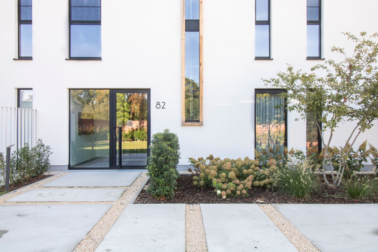 Contemporary white building facade with rectangular windows and landscaped walkway.