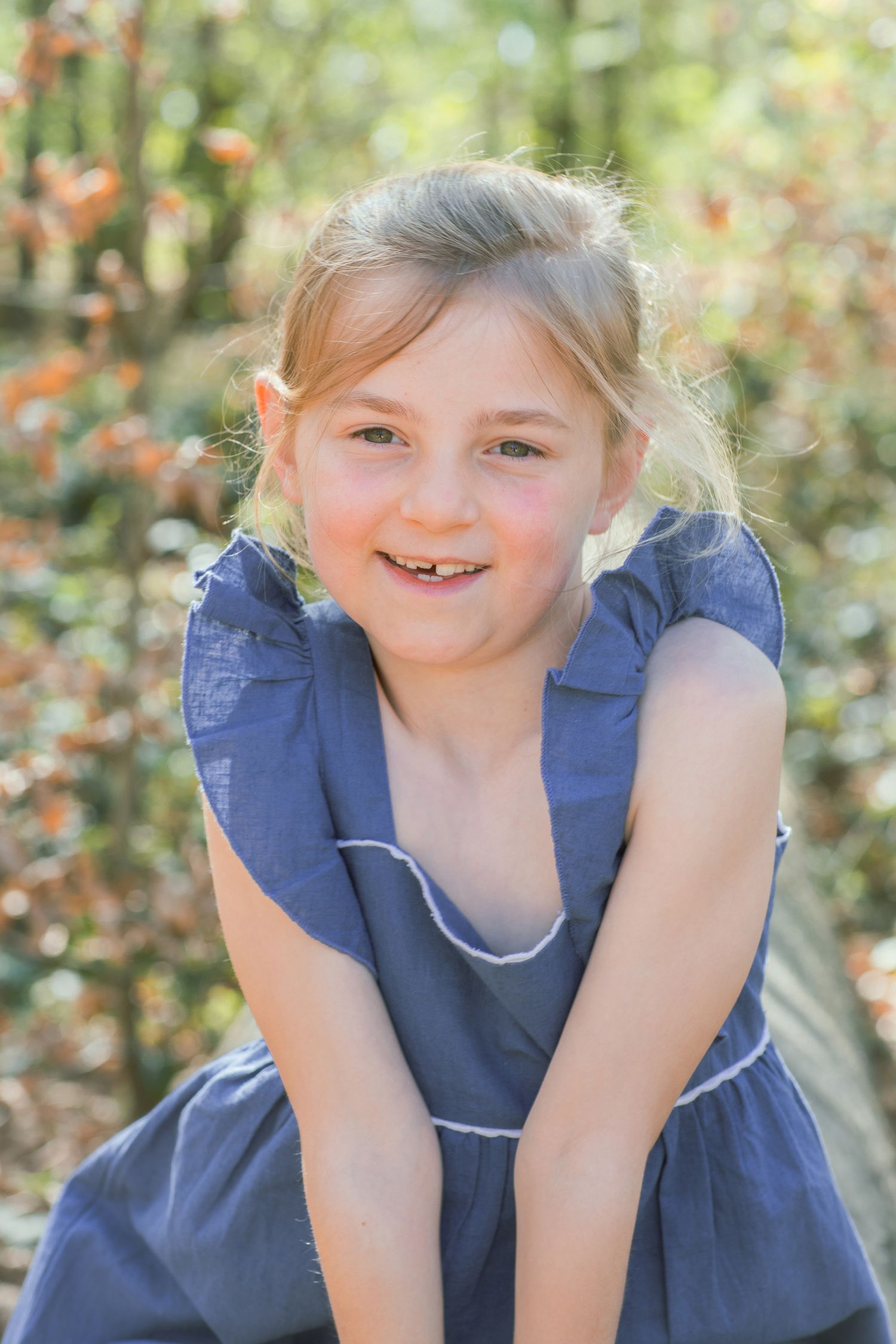Child in blue dress smiling and playing outdoors in natural setting.