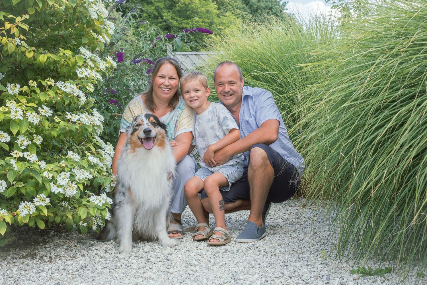 Family and dog posing together on gravel path surrounded by ornamental grasses.