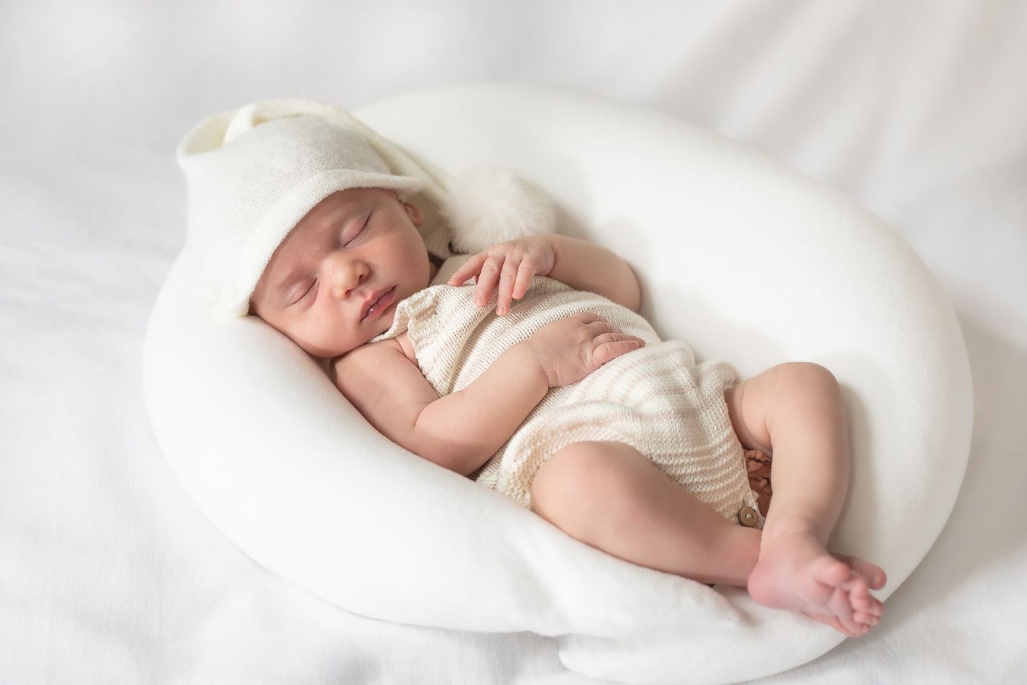 Sleeping newborn wrapped in white fabric on crisp white bedding.