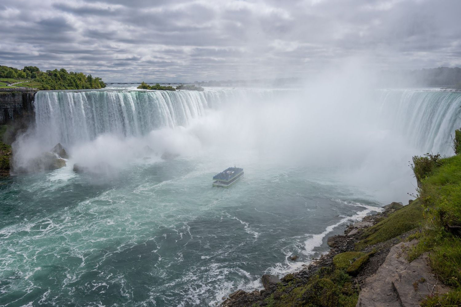 Aerial view of Niagara Falls Horseshoe with a tour boat navigating the misty turquoise waters below.