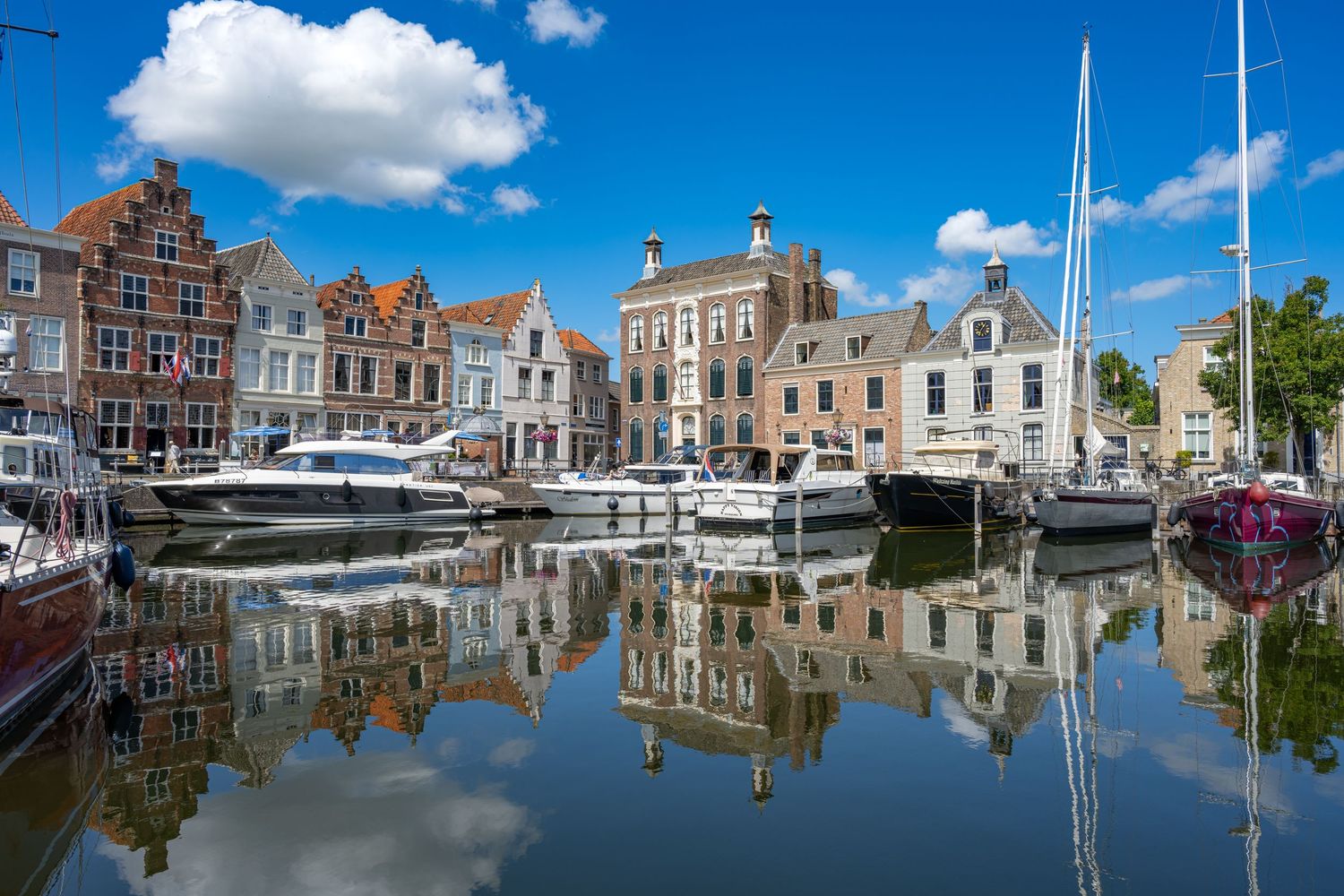 Charming Dutch canal harbor with colorful historic buildings reflecting in calm water with moored boats.