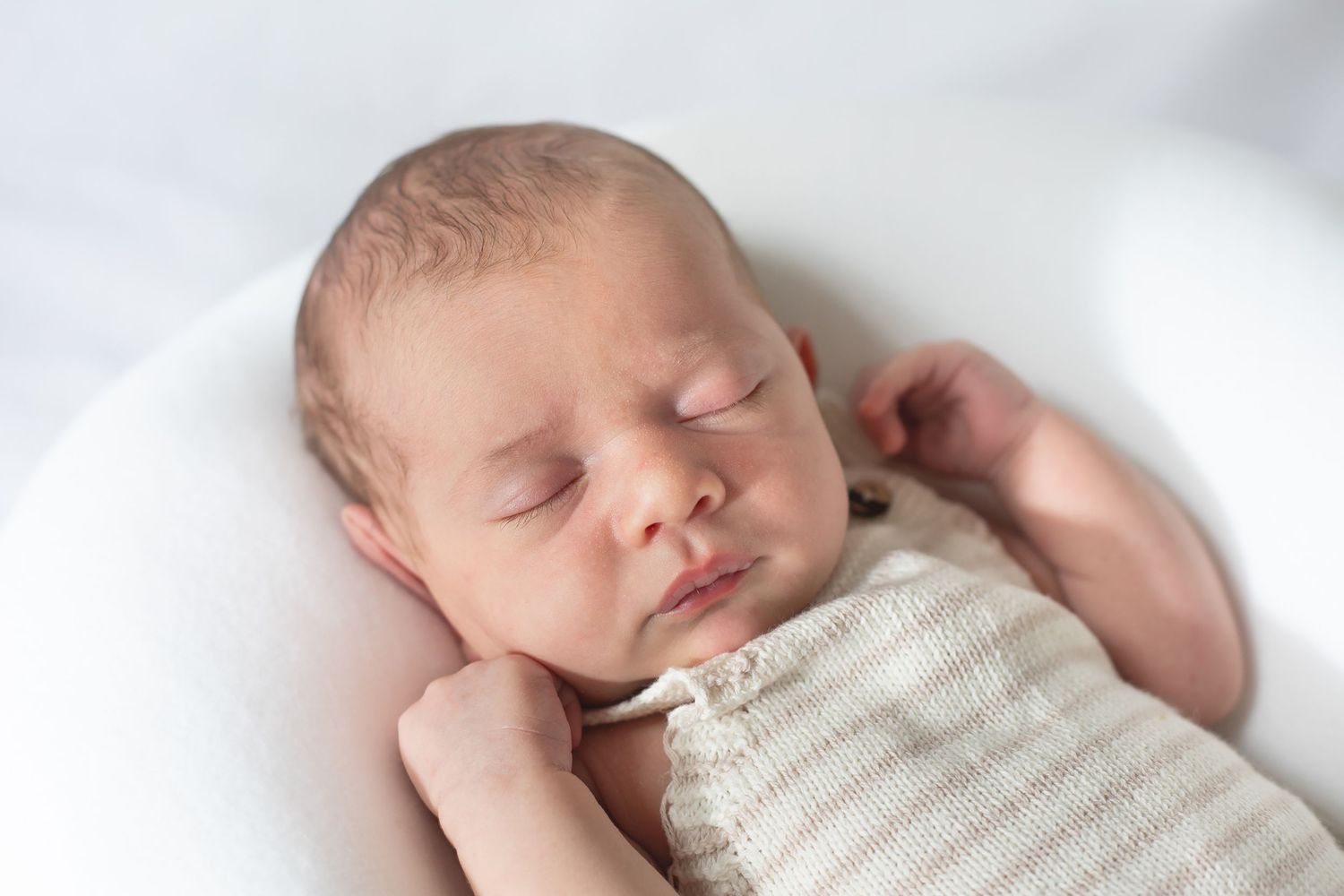 Sleeping newborn wrapped in white blanket on soft white background.