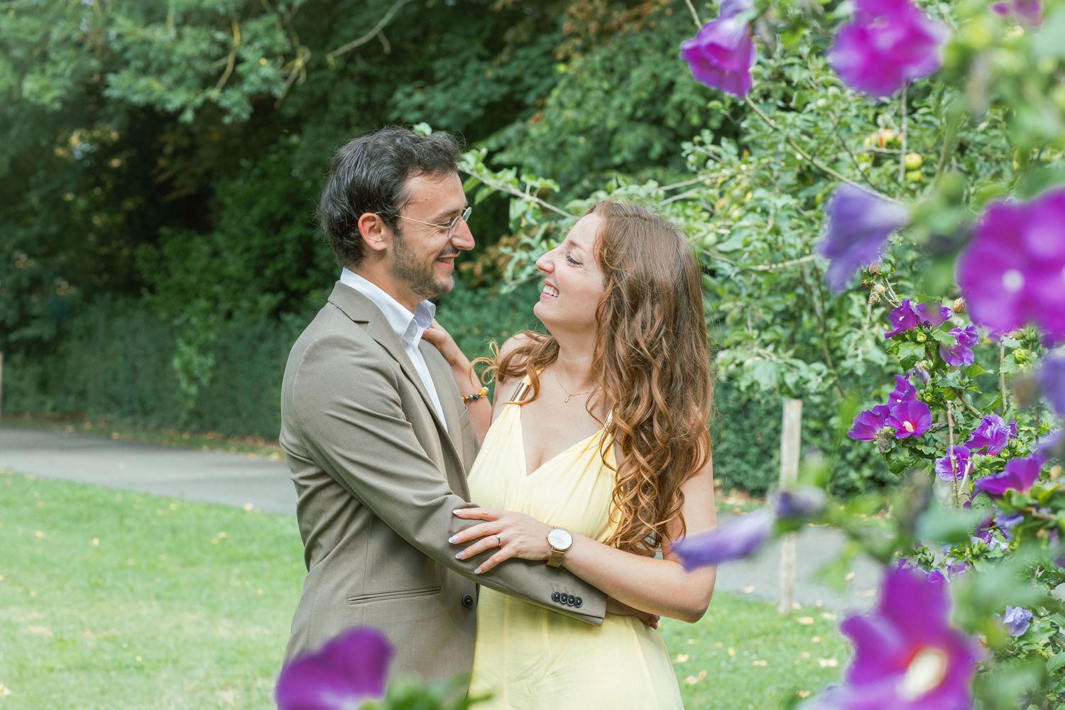 A romantic moment captured in a garden with vibrant purple flowers in the foreground.