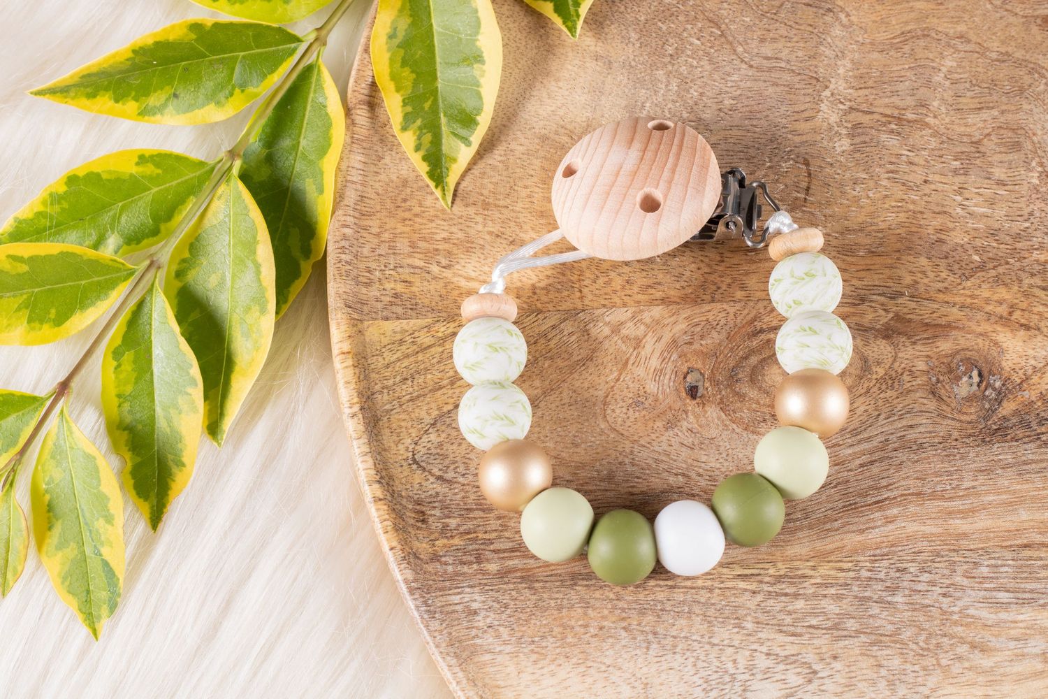 Natural wooden bead necklaces arranged with fresh green leaves on brown wooden background.
