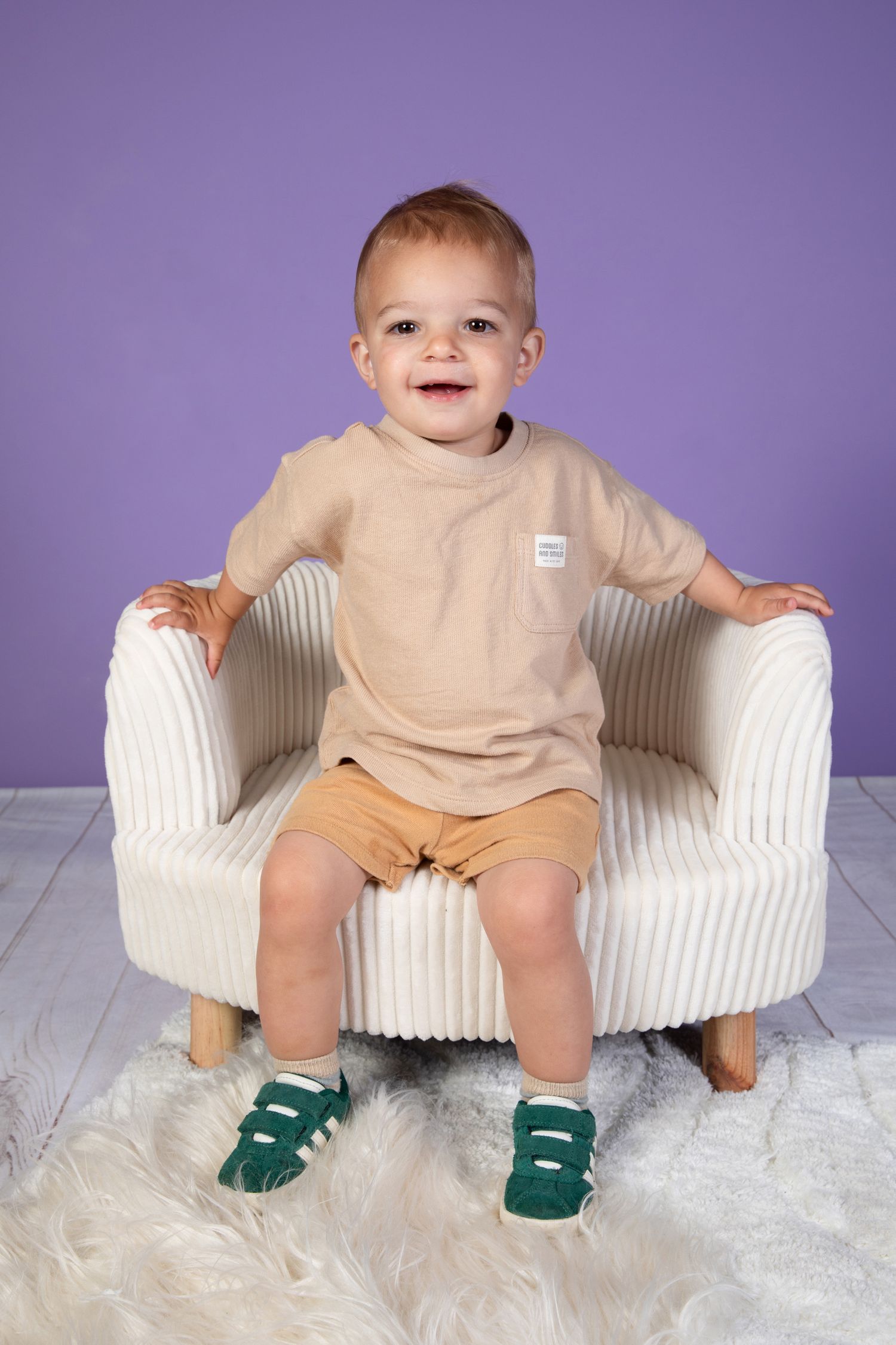 Toddler laughing while seated on white modern chair wearing neutral colored clothing.