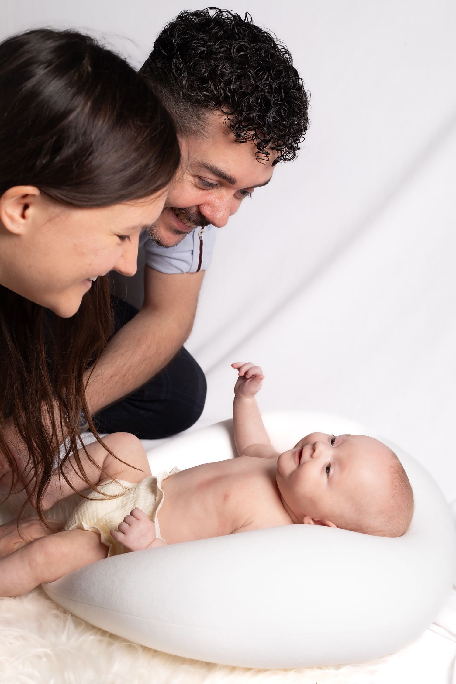 Parents share a tender moment with their baby lying on a white nursing pillow.