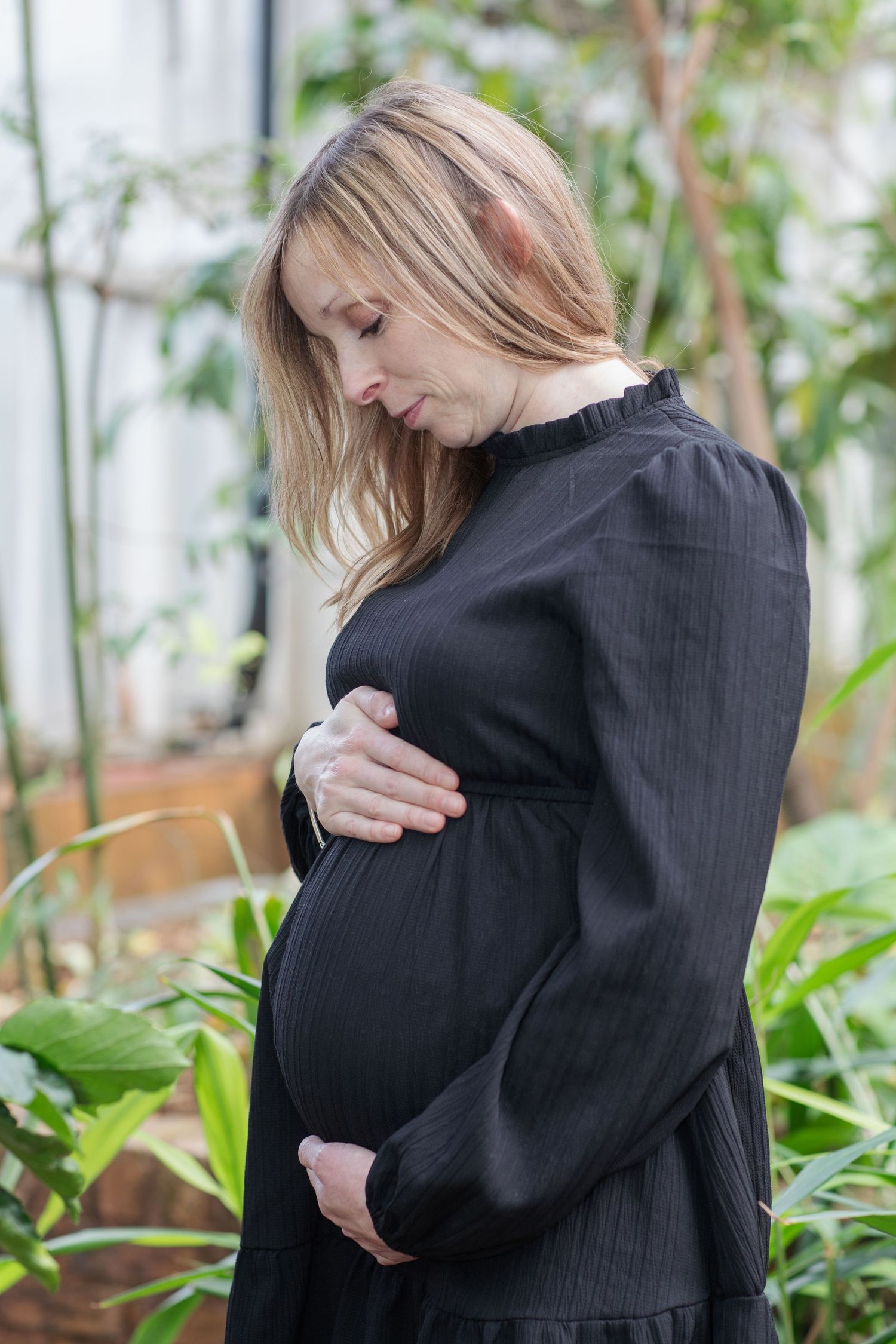 Maternity photo series showing embracing couple in black attire among green plants.