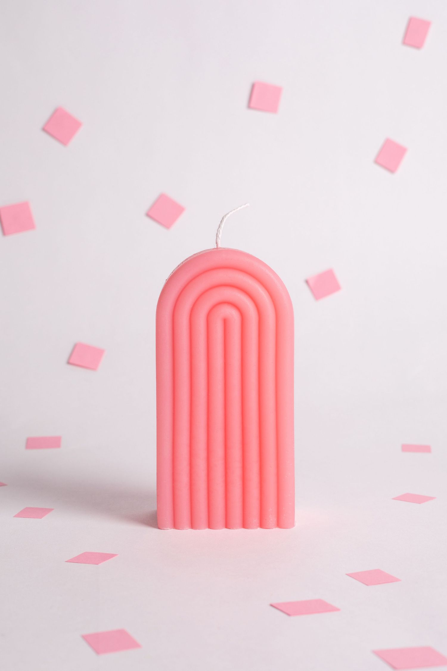 Pink modern arch-shaped candle with scattered pink paper squares on white background.