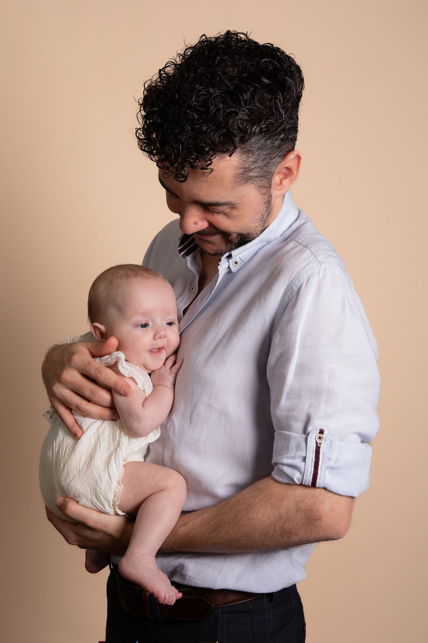 A series of tender moments between an adult in a white shirt holding and embracing a small baby against a neutral background.