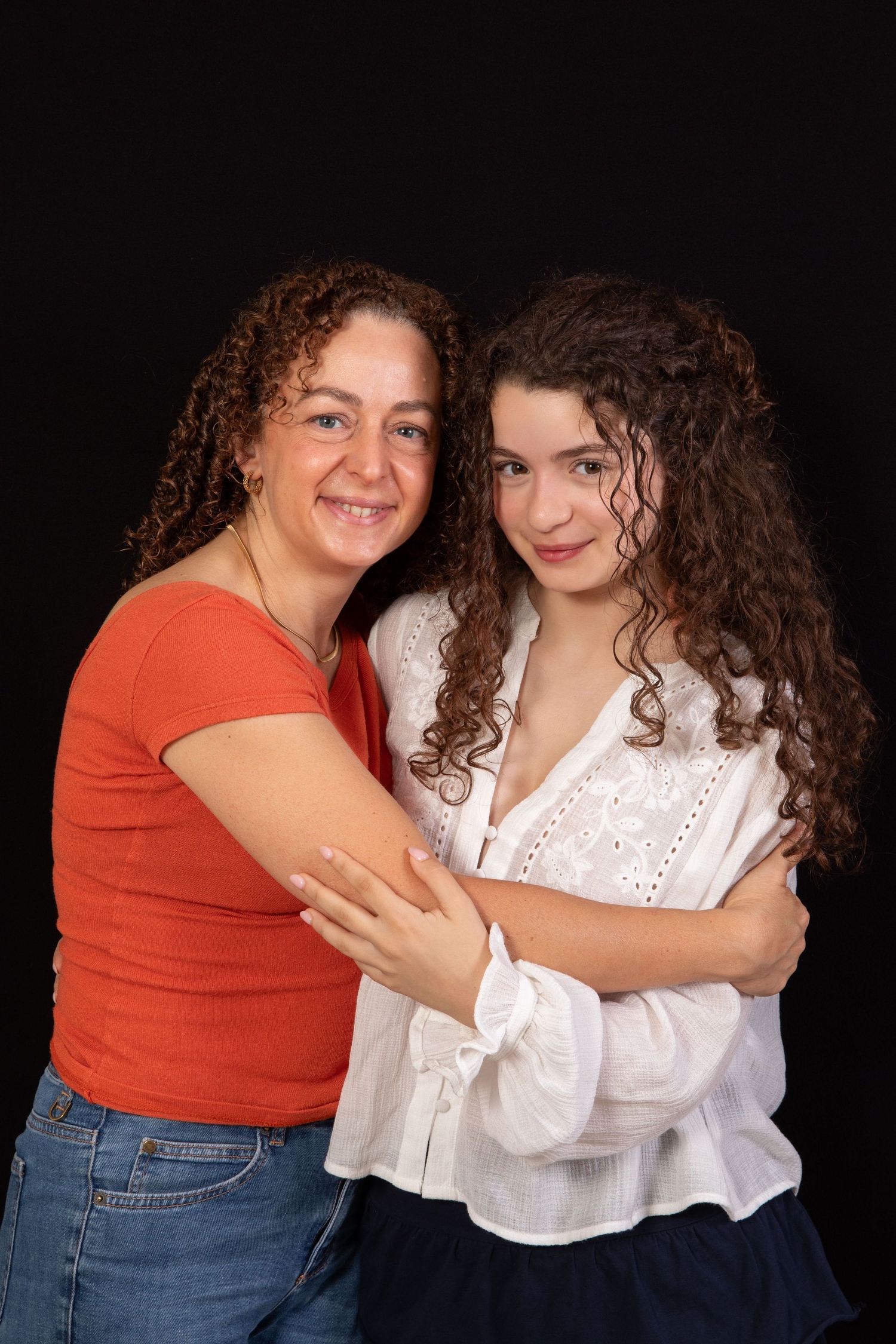 Two people in casual outfits sharing a warm embrace against a dark background.